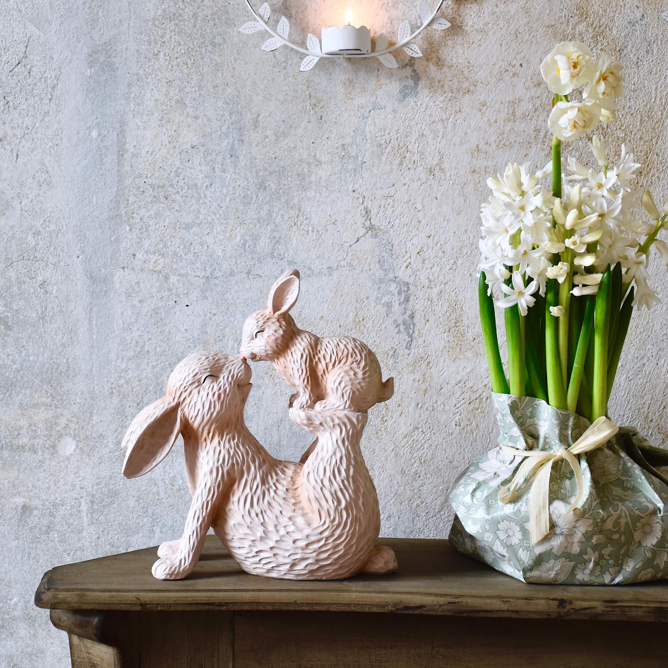 Roze kunststof beeld van twee konijnen op houten tafel naast bloemen in pastelkleurige vaas