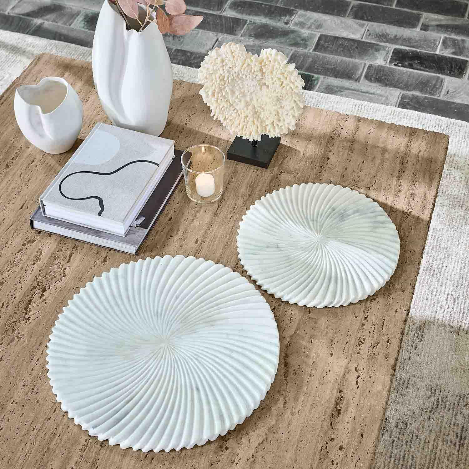 Twee witte marmeren decoratieve borden met golvend patroon op beige tafel met boeken en kaars