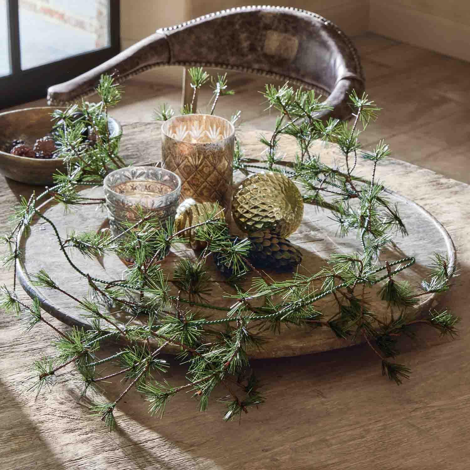 Decoratief houten dienblad met groene takken, gouden versieringen en glazen theelichthouders op tafel