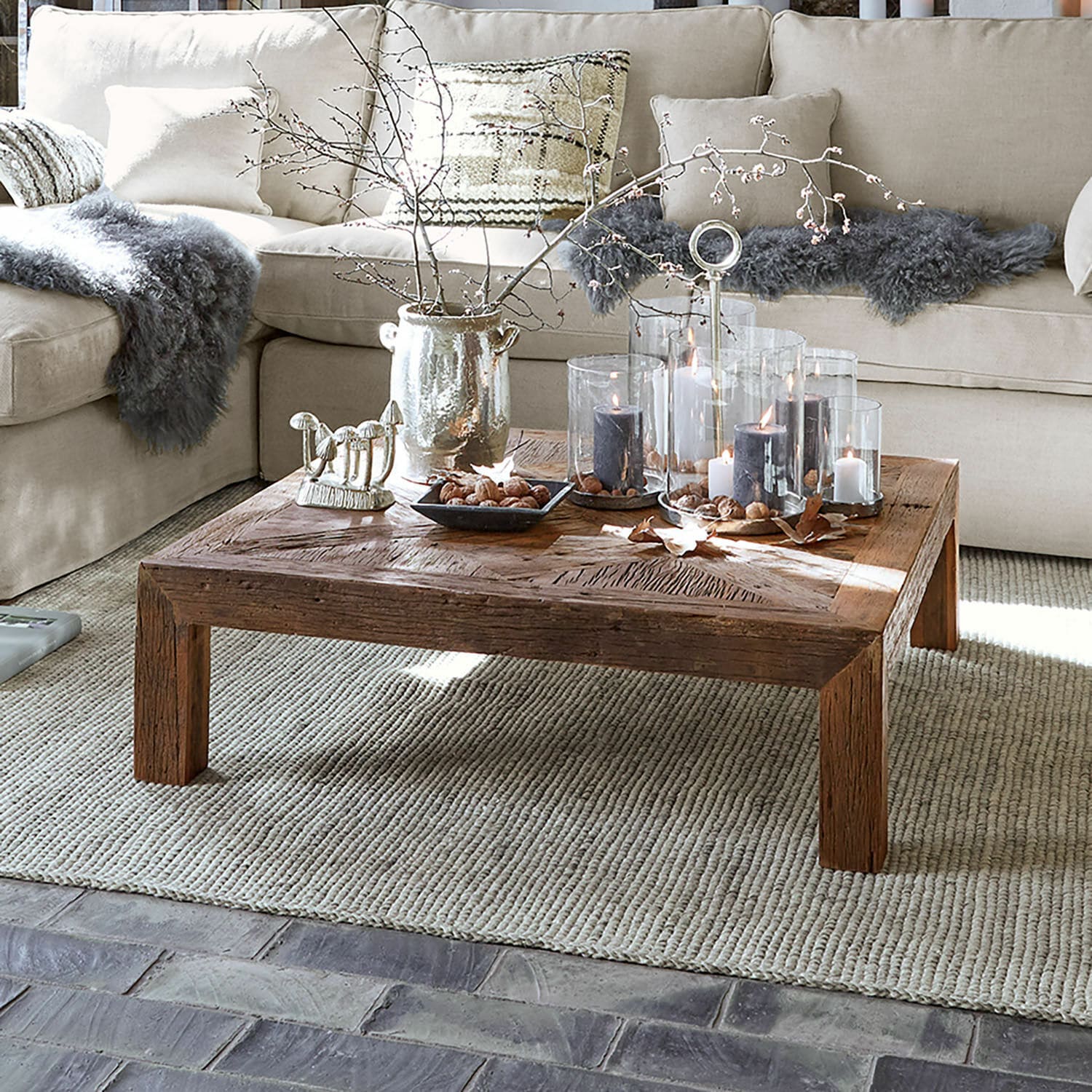 Salontafel Vivacetto Vierkante houten salontafel met decoratieve kaarsen en natuurlijke accenten op een beige vloerkleed