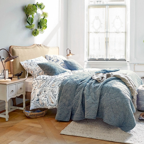 Gezellige slaapkamer met blauw doorgestikt dekbed en beddengoed met patroon op bed met beige hoofdbord