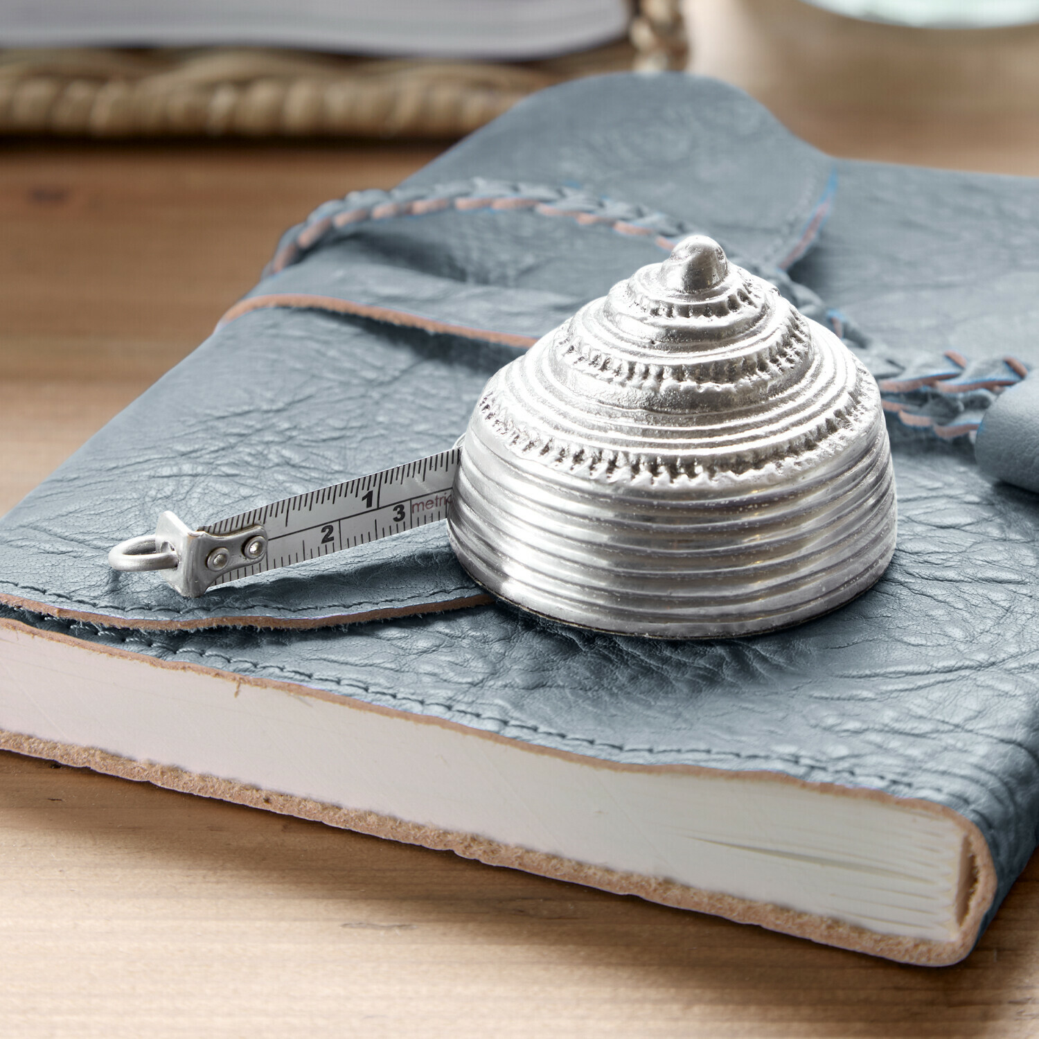 Zilverkleurige metalen meetlint in schelpvorm op een blauw leren notitieboek