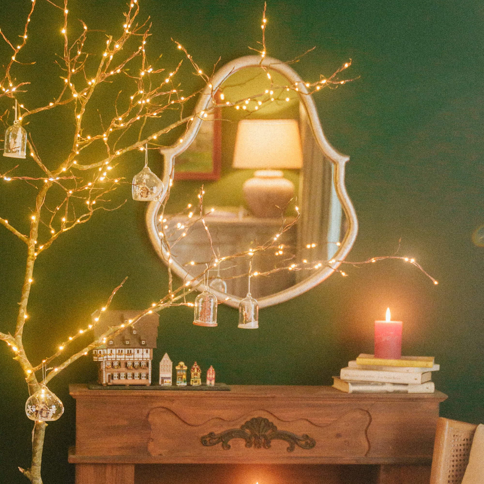 Decoratieve takken met LED-lichtjes en glazen ornamenten voor spiegel en open haard in feestelijk ingerichte kamer