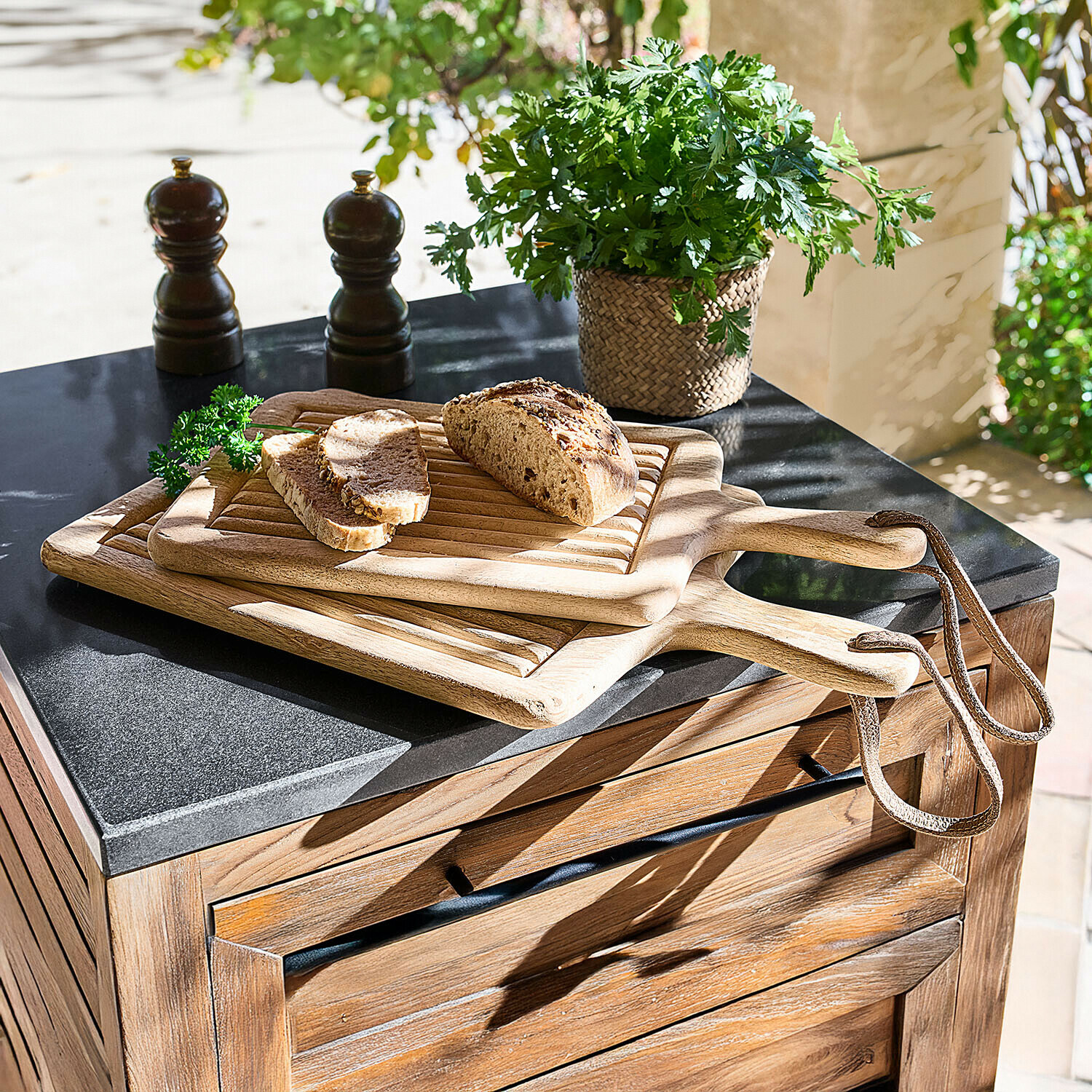 Drie houten snijplanken met handvat en lus, met brood en verse kruiden op een keukenblad