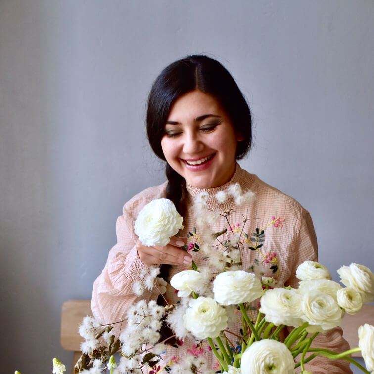 Vrouw in roze geborduurde blouse met witte ranonkels in lichte kamer
