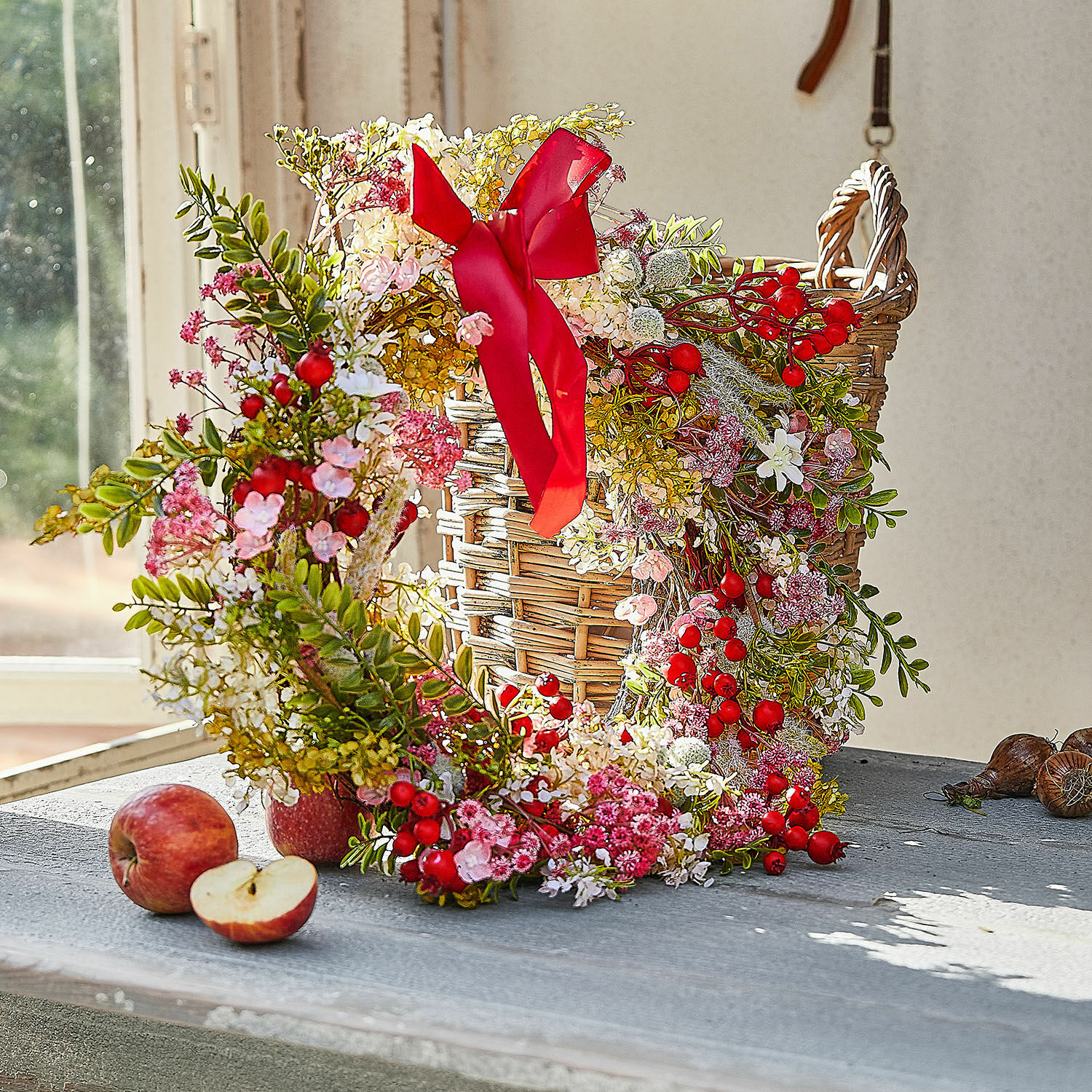 Decoratieve krans met rode bessen en roze bloemen op een rieten mand op tafel