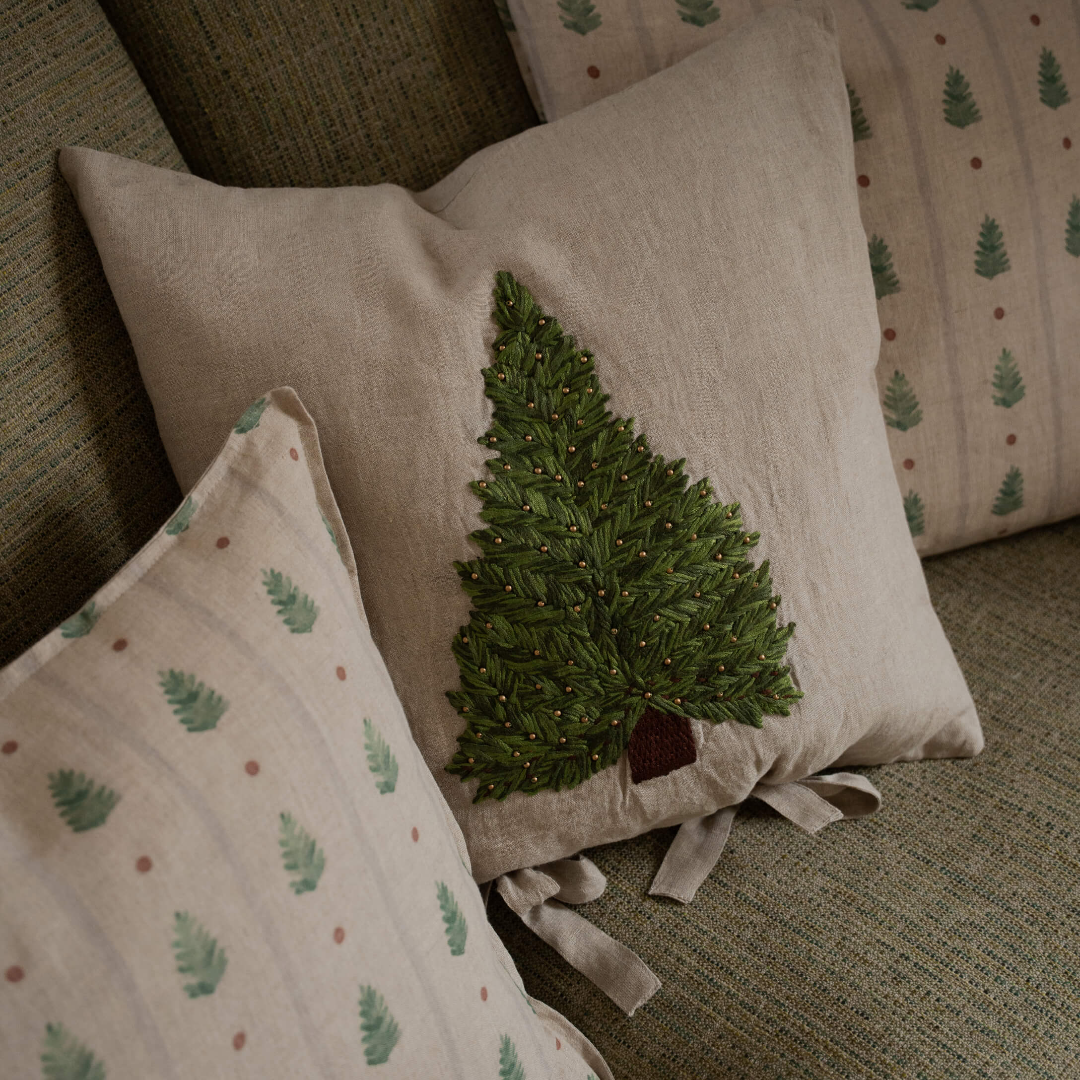 Beige linnen kussen met groen geborduurde boom en decoratieve kralen op een bank