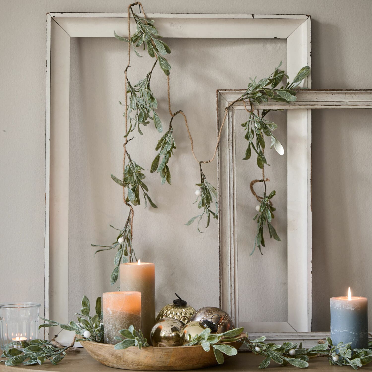 Guirlande Mistletoe Decoratieve slinger met groene bladeren en witte bessen tegen witte houten lijsten, kaarsen en decoraties
