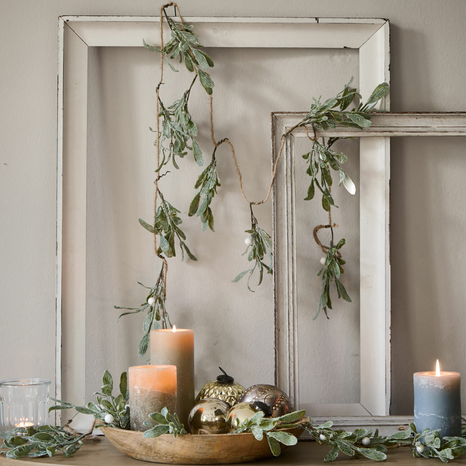 Guirlande Mistletoe Decoratieve slinger met groene bladeren en witte bessen tegen witte houten lijsten, kaarsen en decoraties
