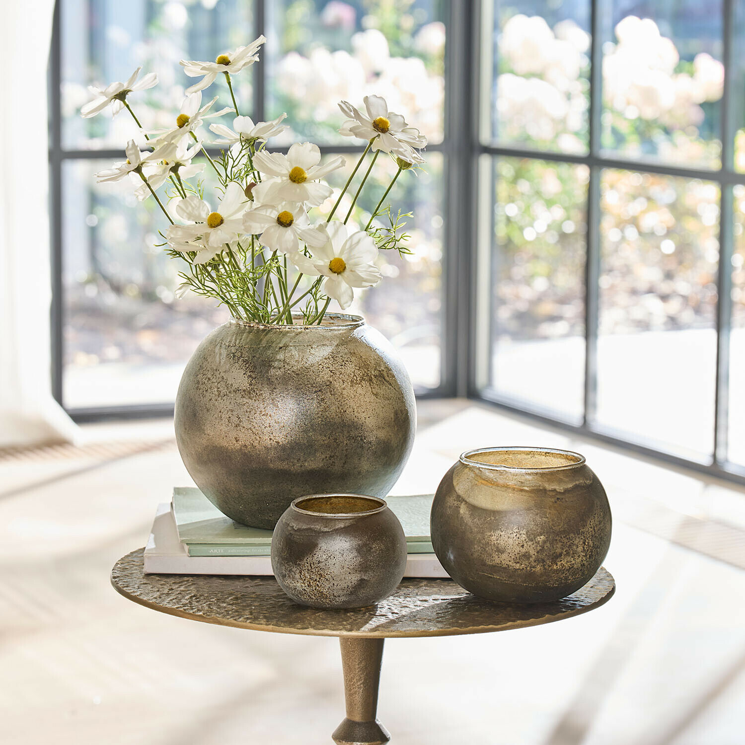 Set van drie ronde glazen vazen in antiek goud op tafel met bloemen en boeken