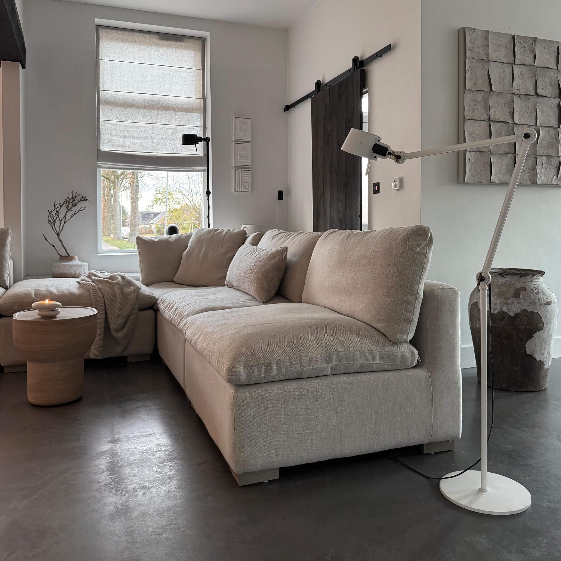 Beige stoffen hoekbank in moderne woonkamer met staande lamp en houten bijzettafel