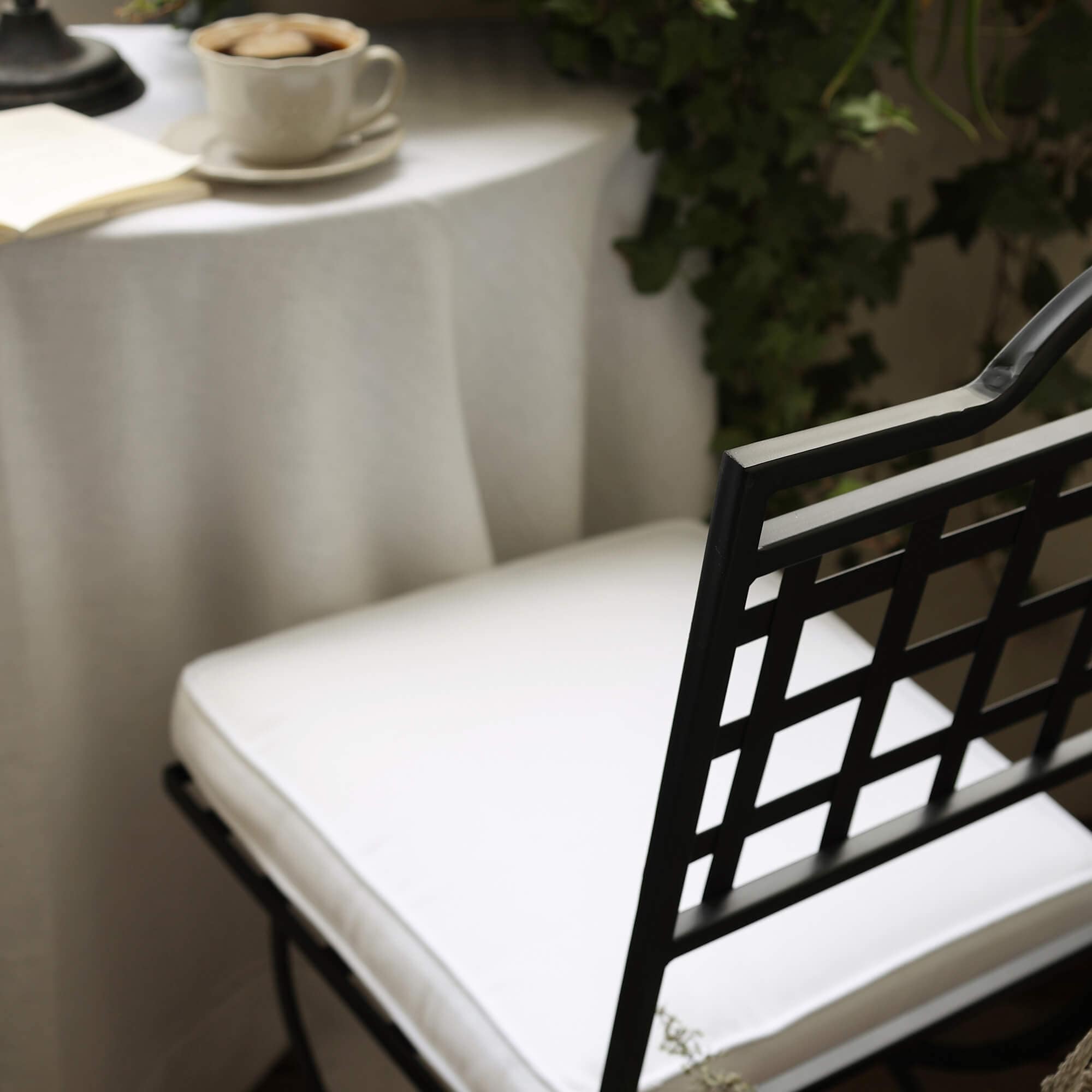Zwarte metalen stoel met wit kussen bij tafel met koffiekopje en groene planten op balkon