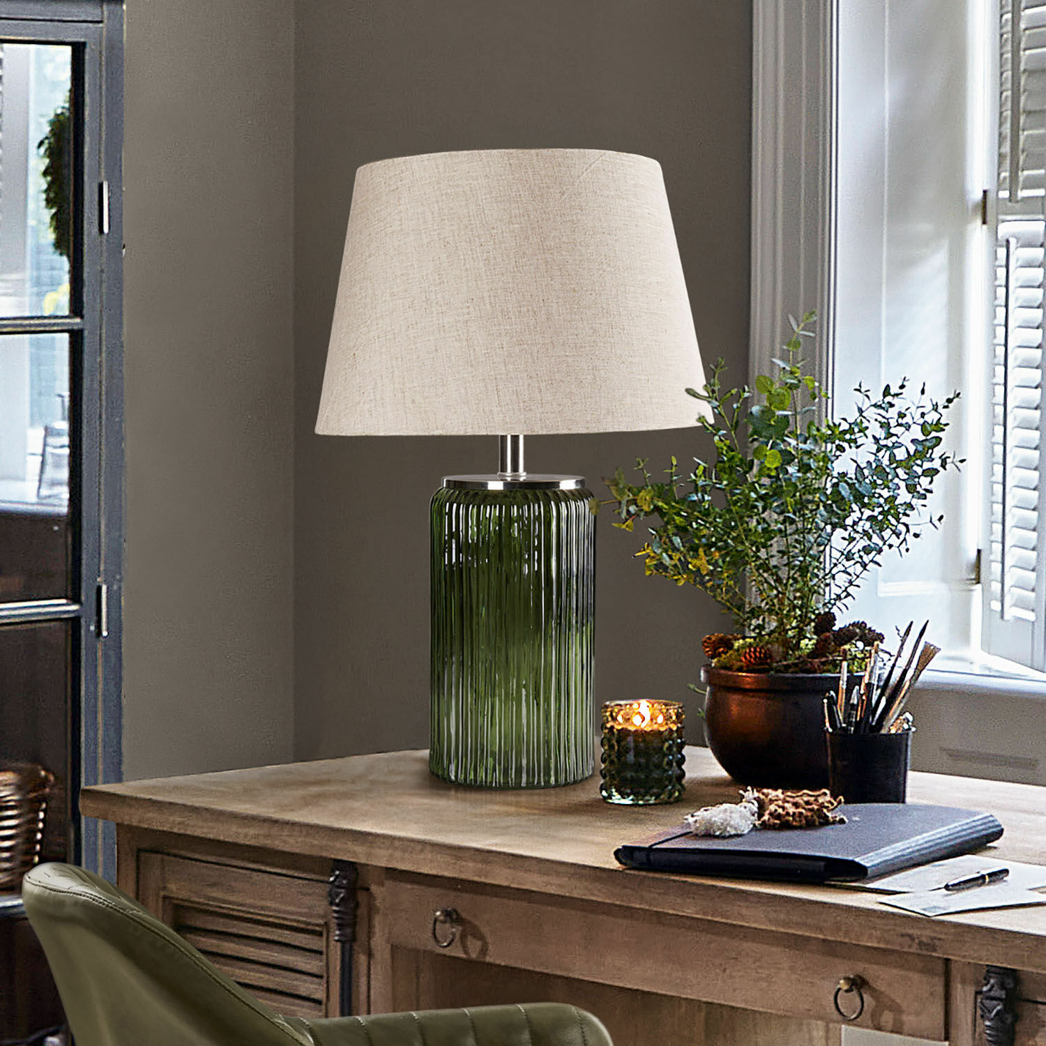 Tafellamp van groen glas met beige kap op vintage houten bureau