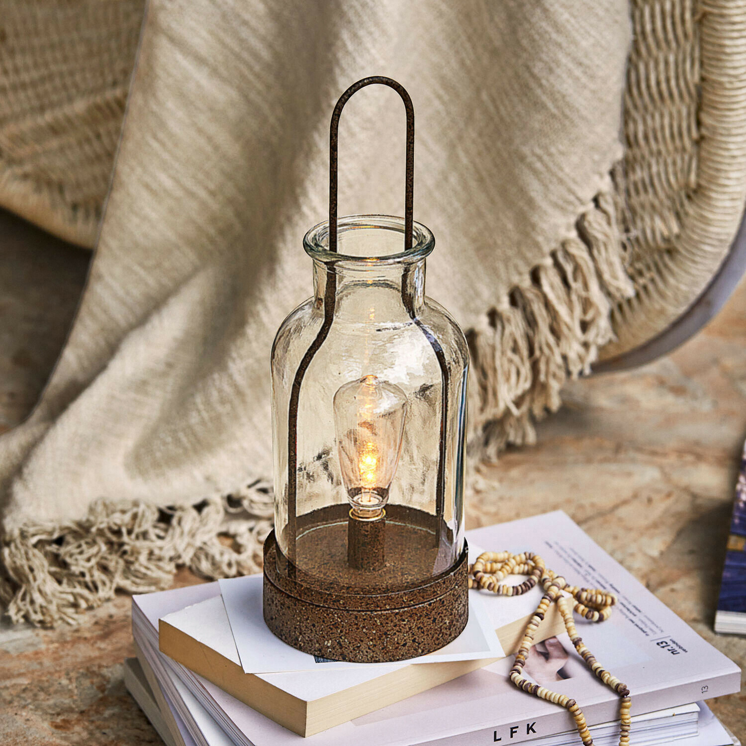 Glazen lantaarn met roestkleurige metalen voet, decoratieve tafellamp op boeken