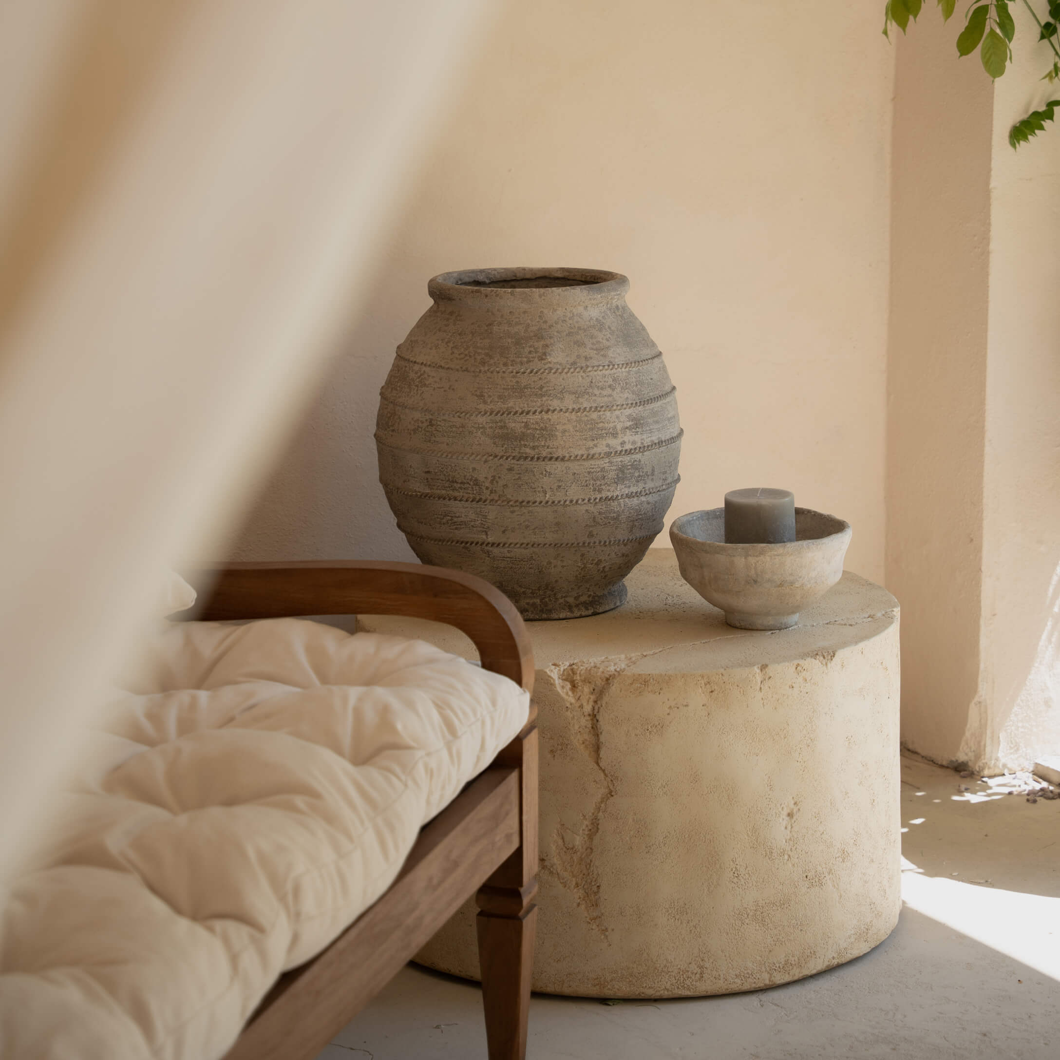 Ronde stenen tafel met grijze keramische vaas en kaars in lichte ruimte met houten bank