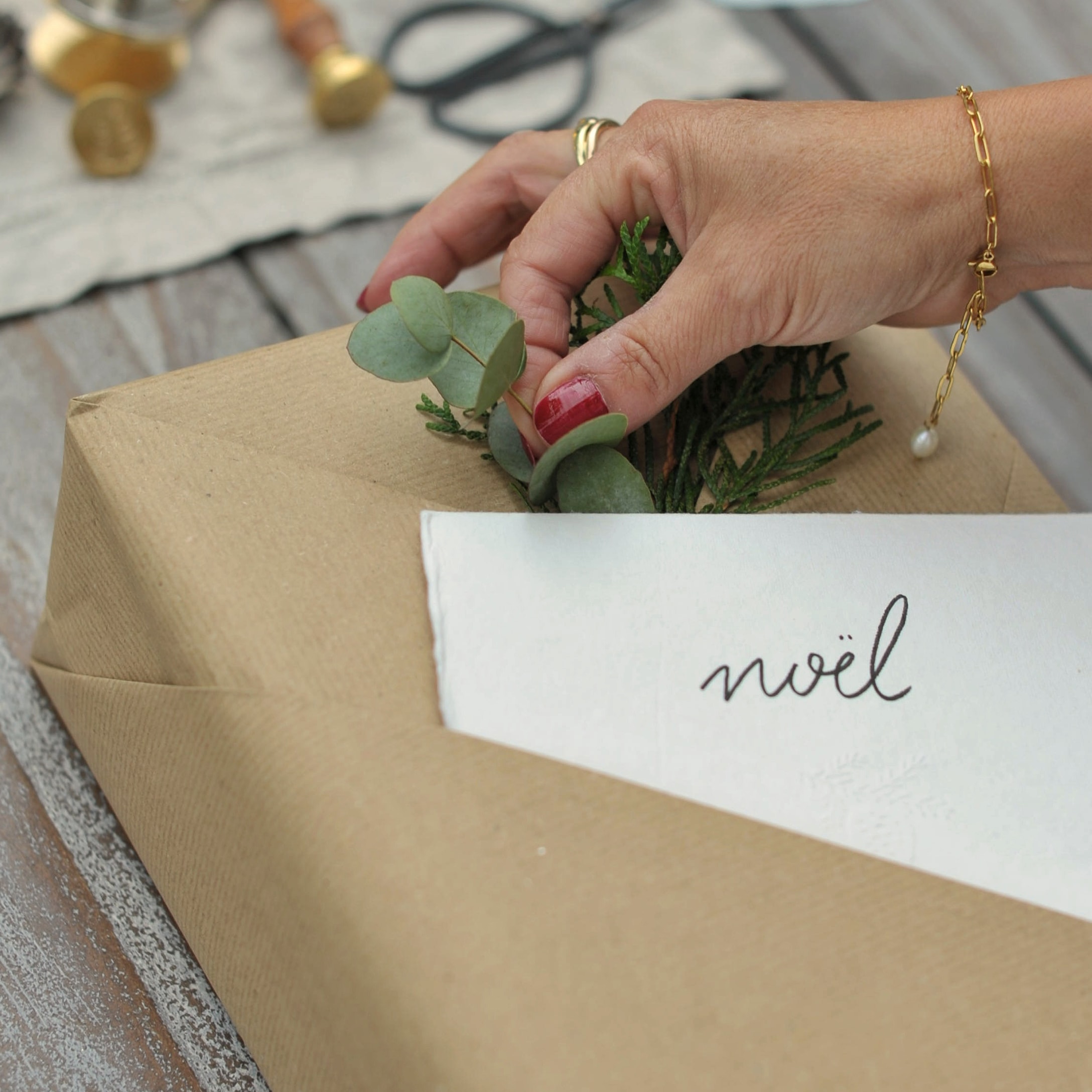 Hand die cadeau in bruin papier versiert met groene bladeren en noël kaart