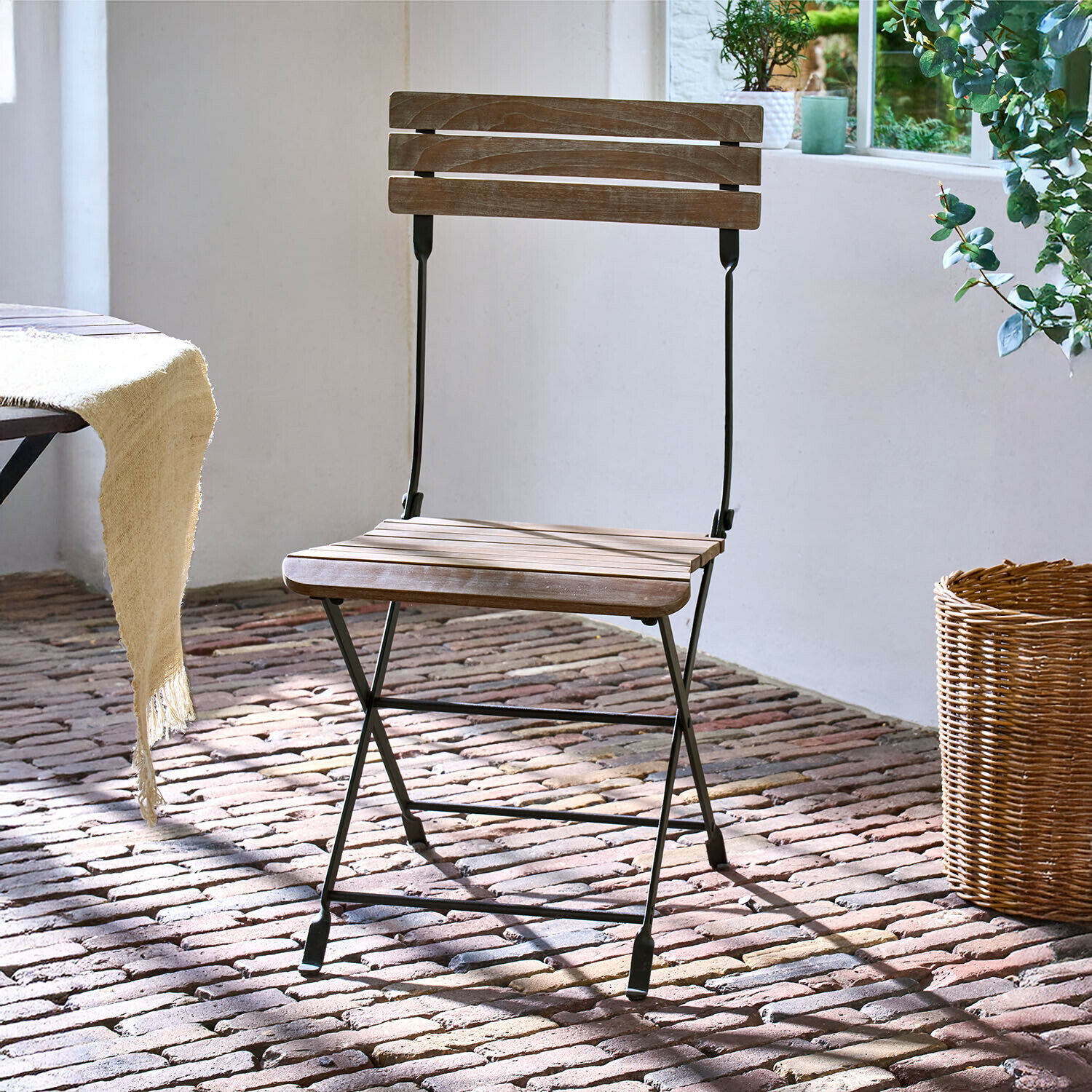 Opvouwbare houten stoel met zwart metalen frame op bakstenen vloer bij natuurlijk licht