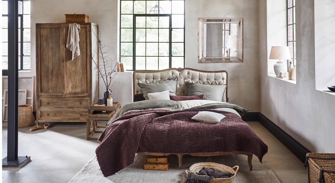 Gezellige slaapkamer met houten kast, gestoffeerd bed en bordeauxrode zachte textieldeken