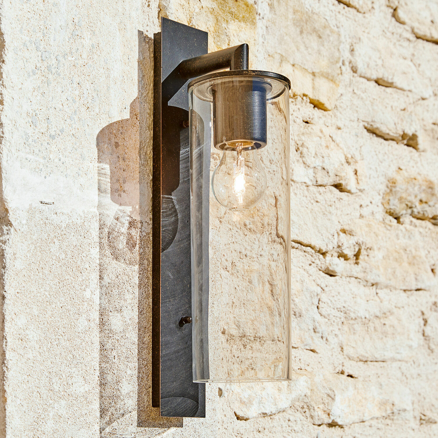 Buitenlamp Clisson Zwarte metalen wandlamp met doorzichtige glazen kap aan lichte stenen muur buiten