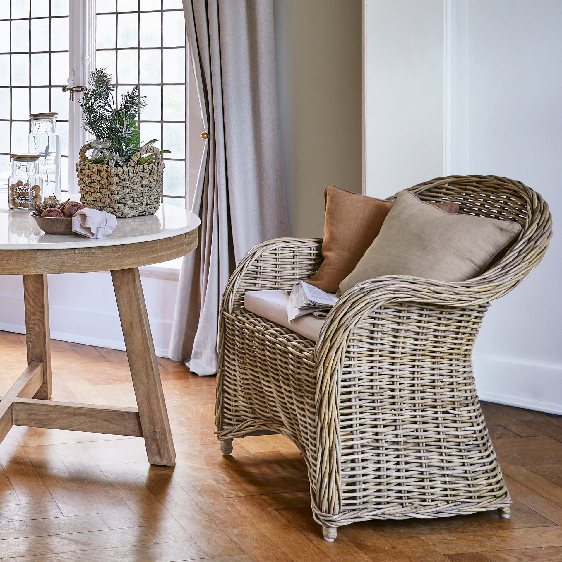 Natuurlijke rotan stoel met beige kussens in lichte woonkamer met houten vloer
