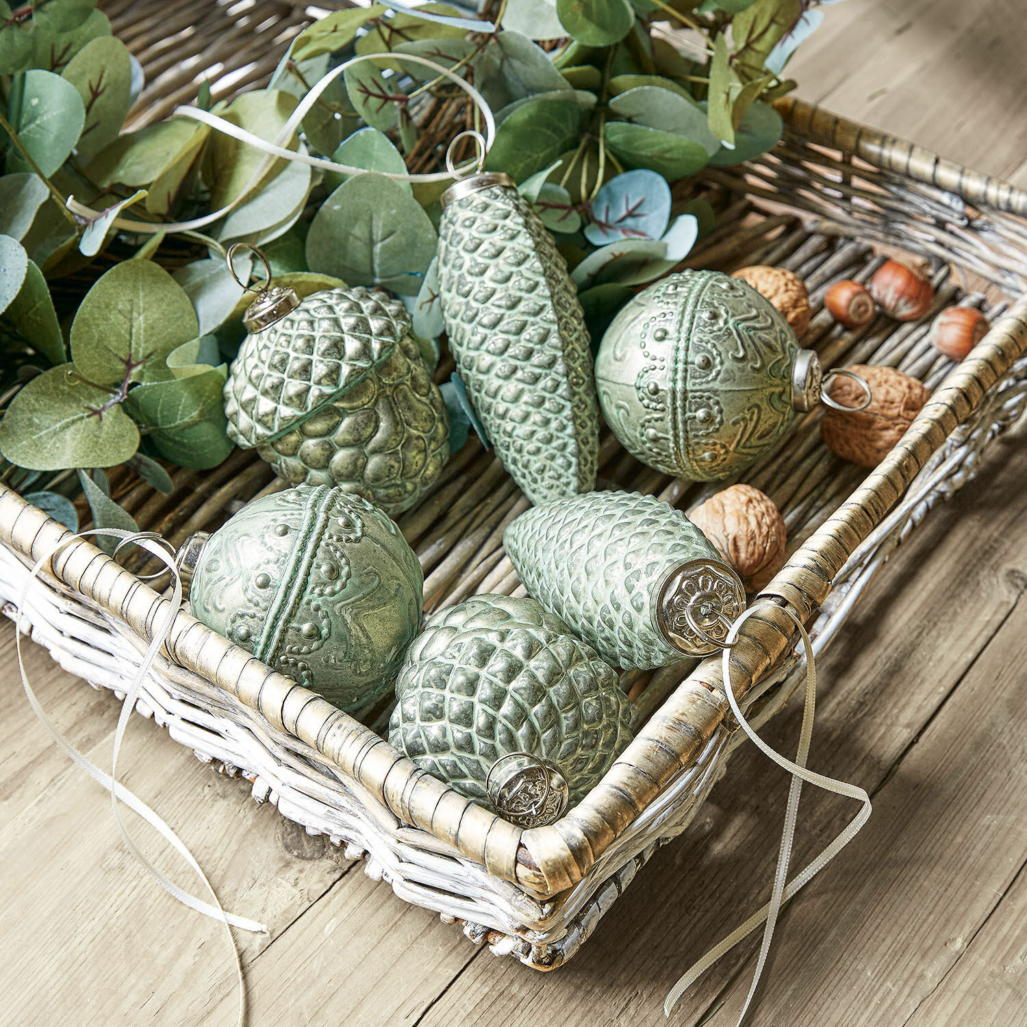 Groene kerstversieringen in dennenappel- en eikelvorm in een rieten mand op een houten tafel