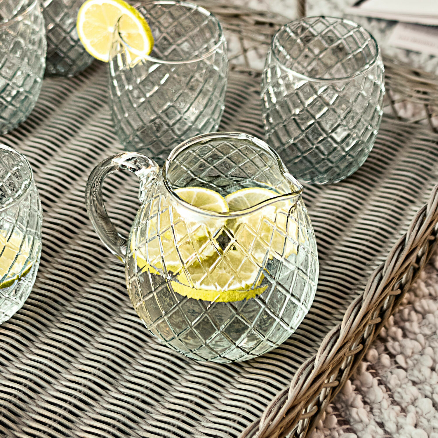 Glazen karaf en glazen met ruitpatroon op dienblad met citroen, perfect voor dranken.