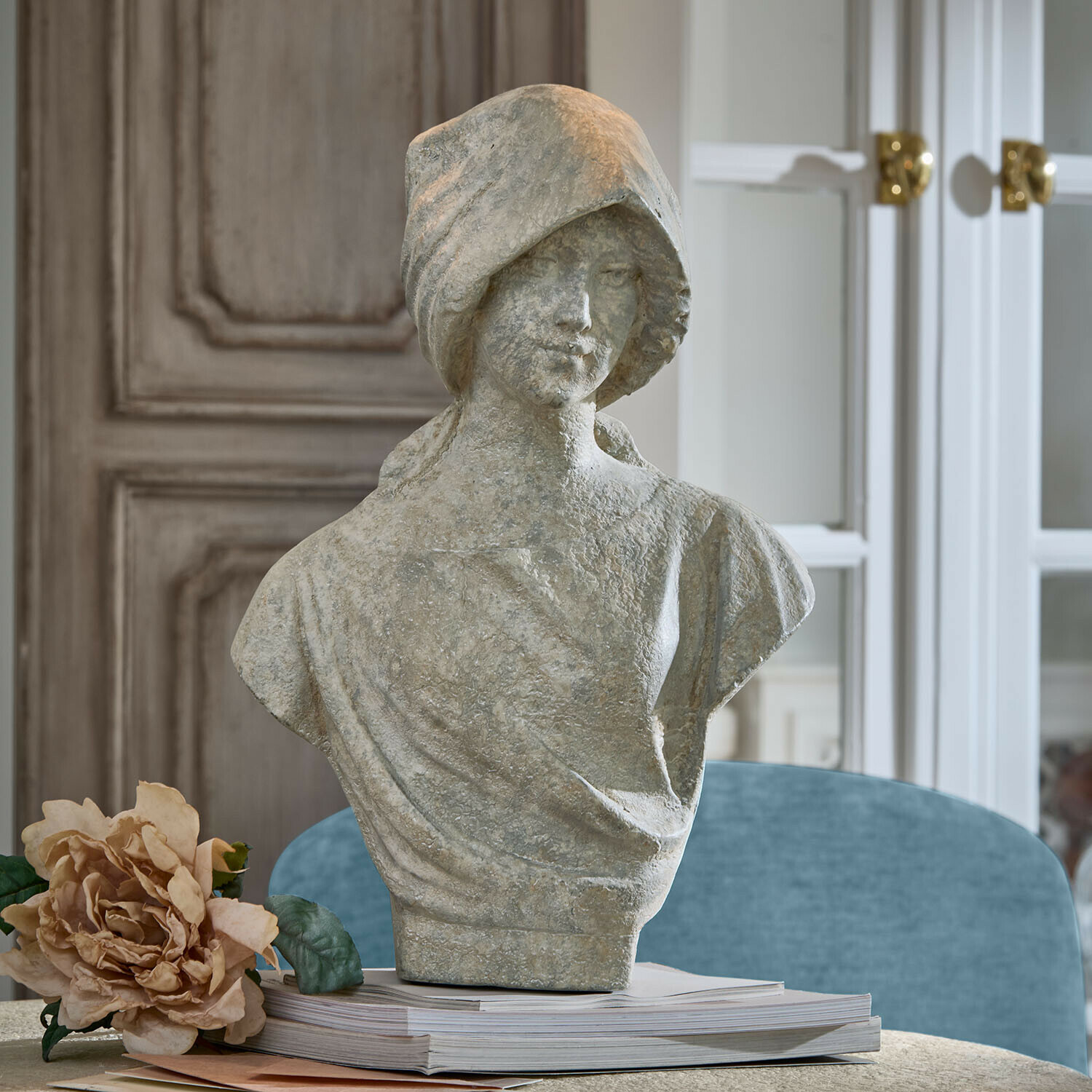 Grijs stenen vrouwenbuste op stapel boeken met decoratieve bloem ernaast in interieur
