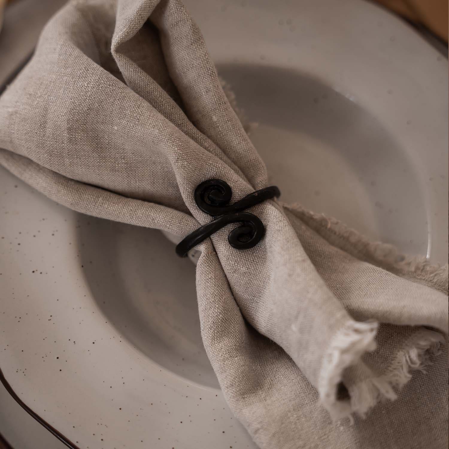 Beige linnen servet met zwarte metalen servetring op lichte bord
