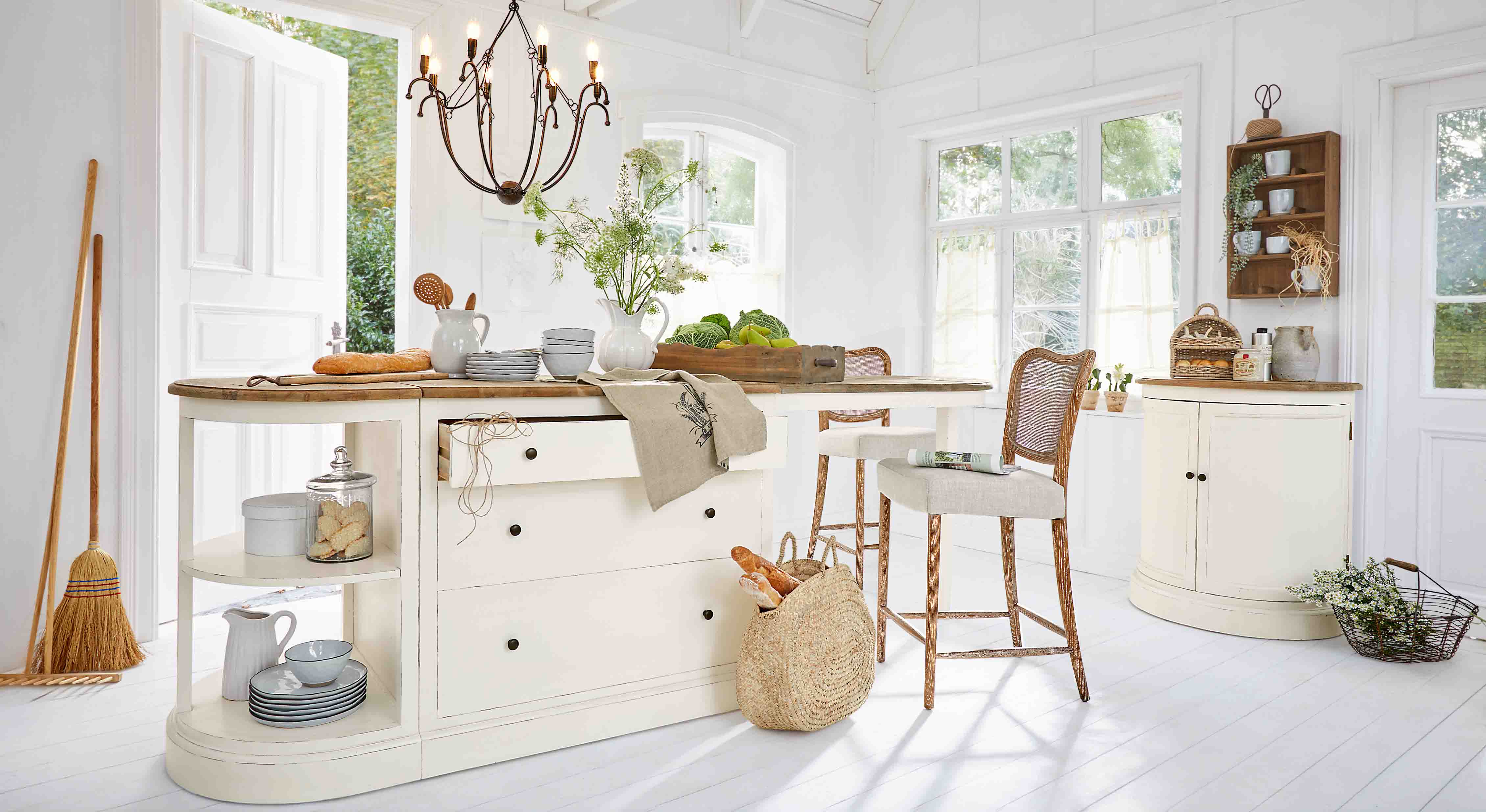 Lichte keuken met wit eiland en houten blad, rotan stoelen en natuurlijke decoraties