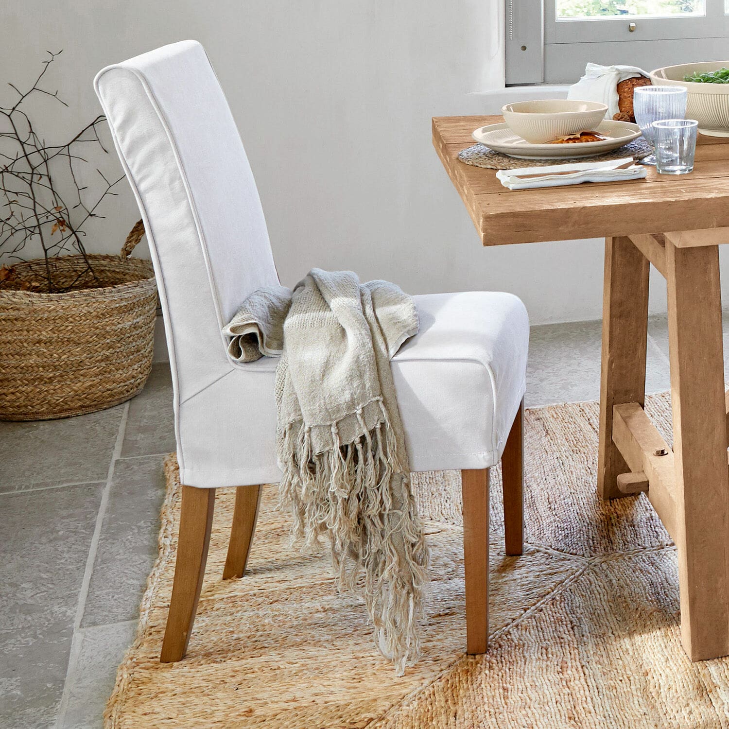 Witte gestoffeerde stoel met houten poten en beige deken op natuurlijke jute vloerkleed