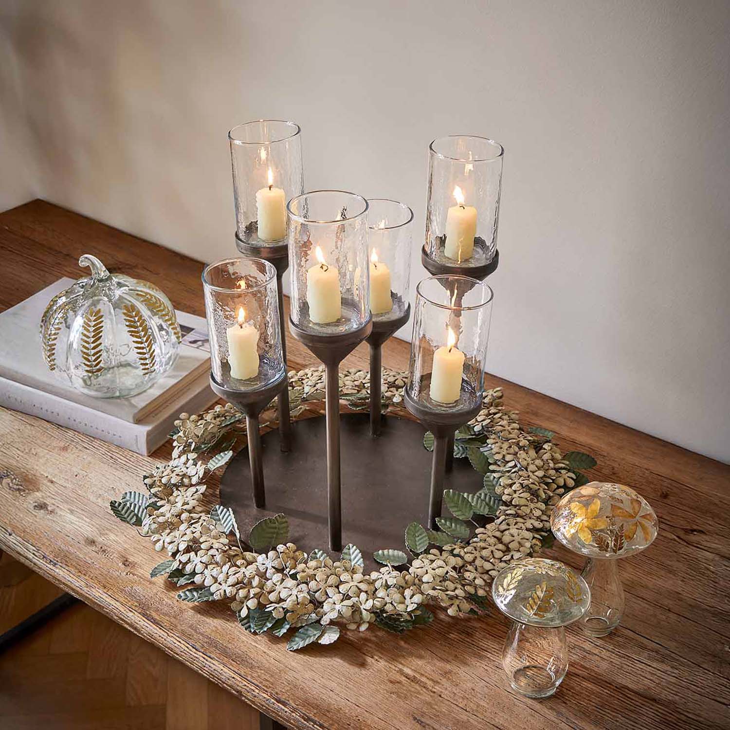 Metalen kandelaar met zes glazen houders en witte kaarsen op houten tafel met bloemendecoratie