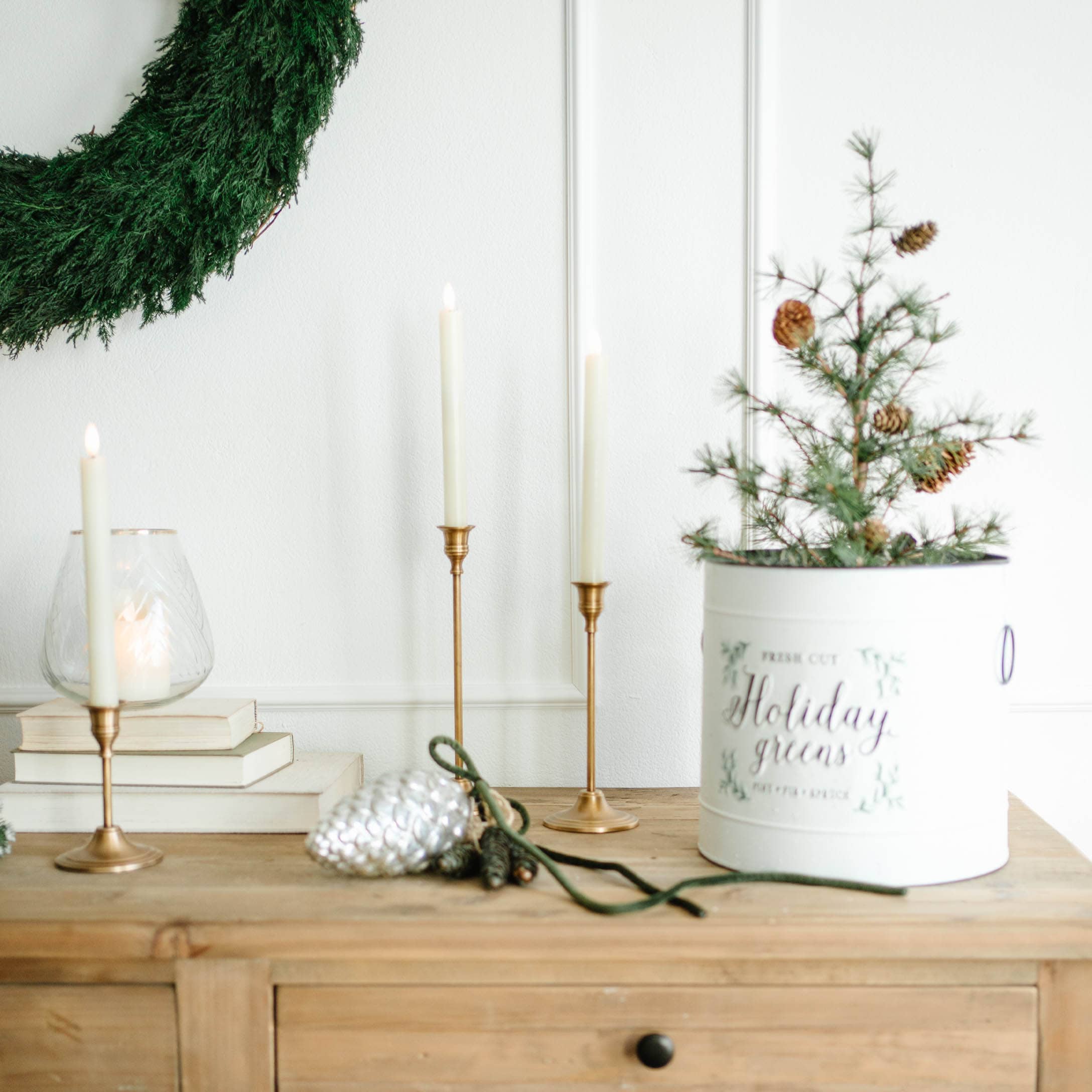 Kerstdecoratie met groene krans, gouden kandelaars en witte pot met takken en dennenappels