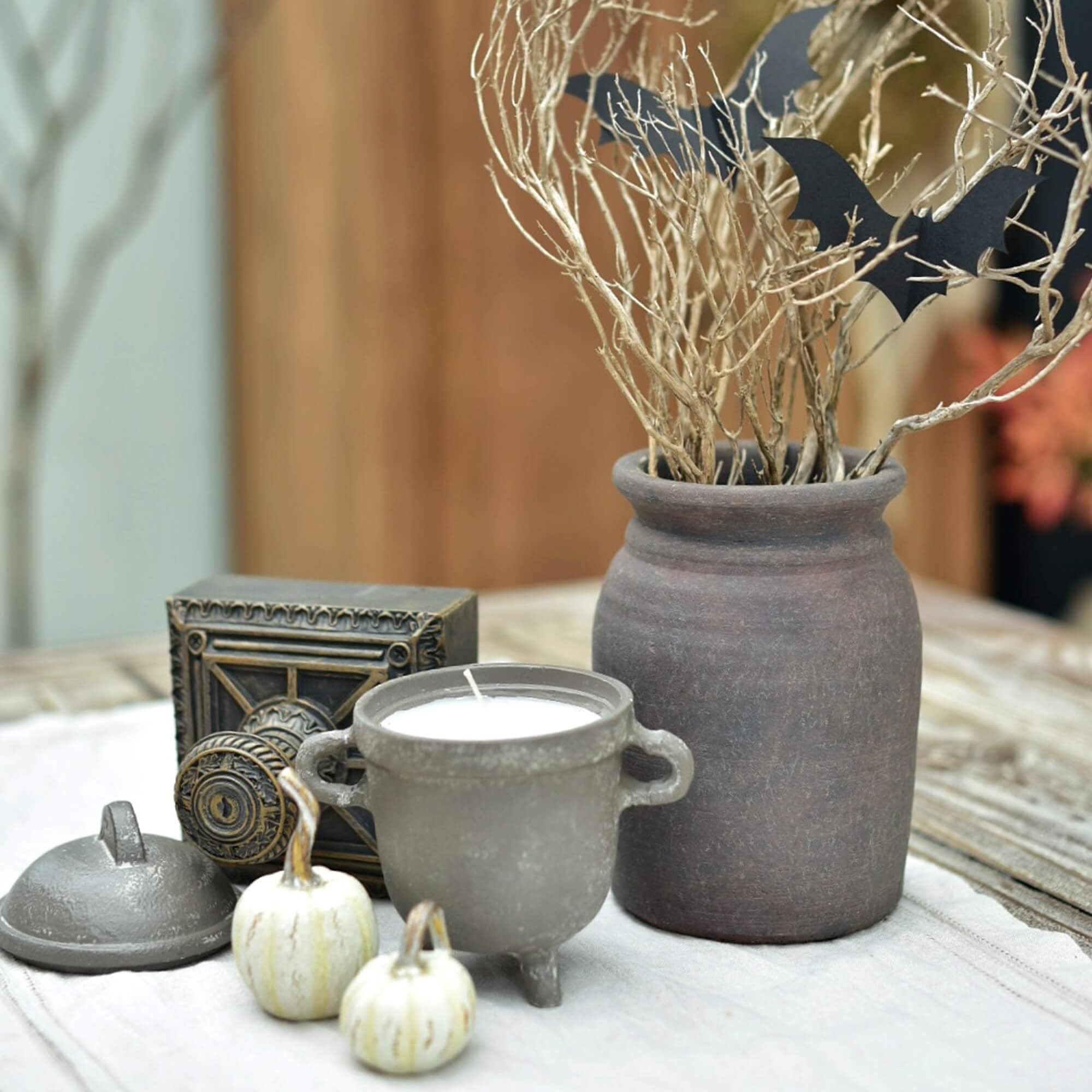 Decoratieve set met keramische kaars, aardewerken vaas en witte mini-pompoenen op tafel