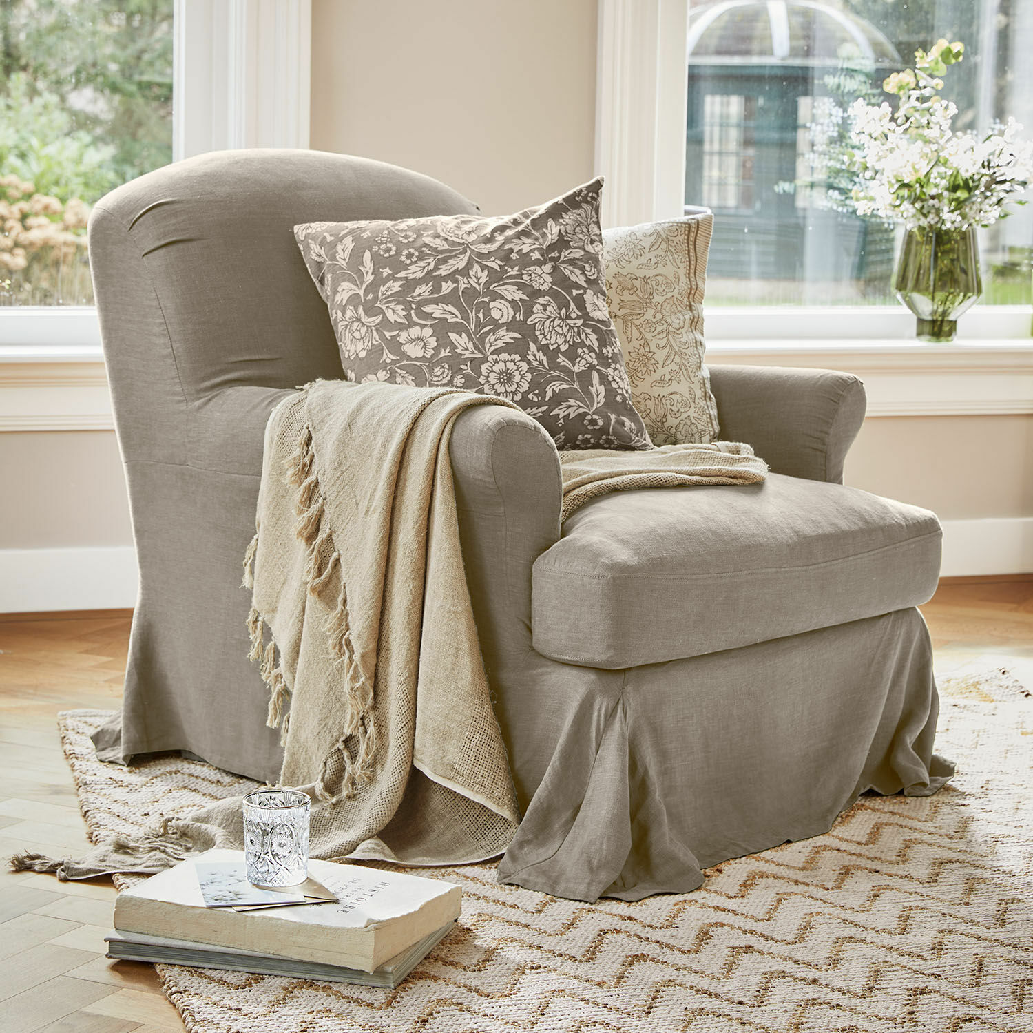 Leunstoel Vionnique Beige stoffen fauteuil met decoratieve kussens en deken op lichte vloerkleed in woonkamer