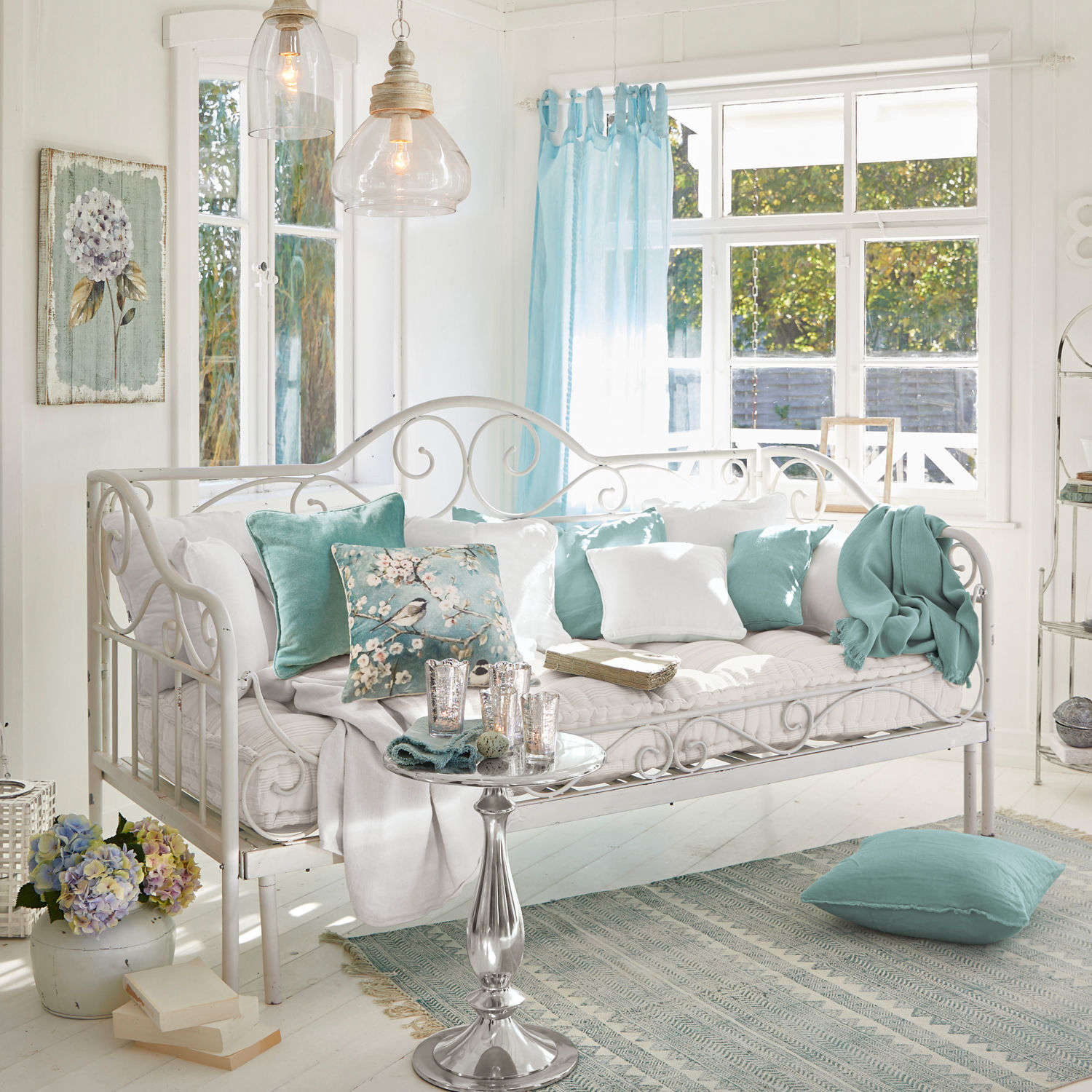 Bedbank Maditha Witte metalen bank met zachte kussens en turquoise accenten in lichte woonkamer met groot raam