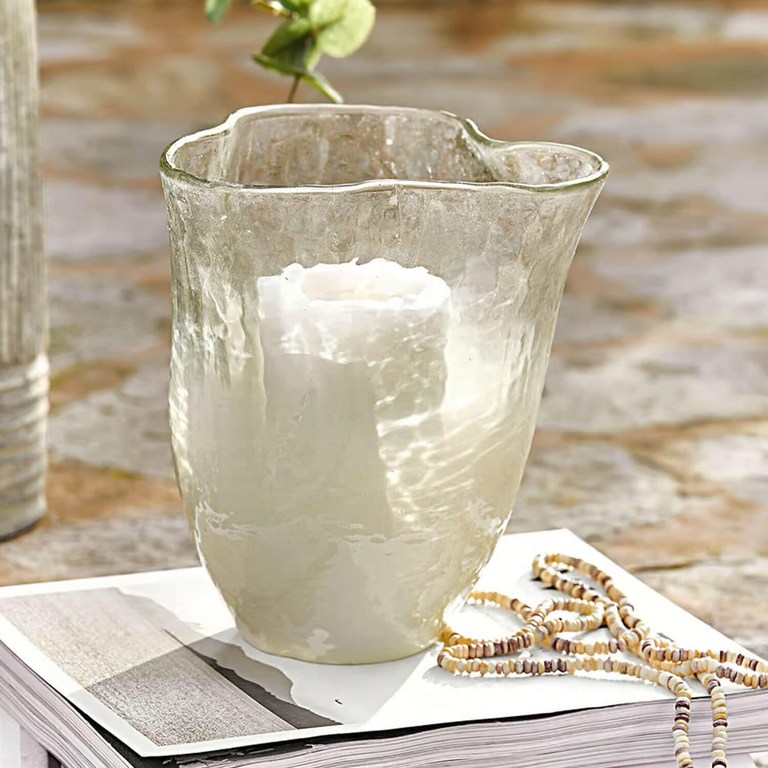 Transparante glazen windlicht met witte kaars op boek met decoratieve ketting