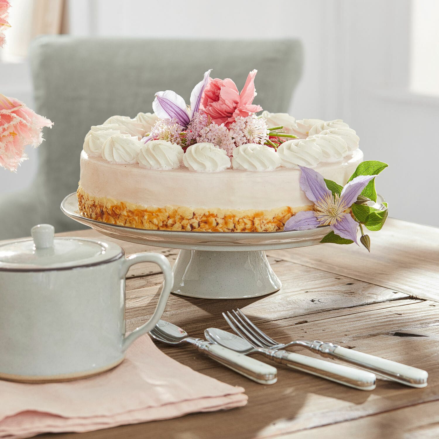 Schaal Biarré Taart op keramische schaal met room en bloemen, bestek met witte handvatten op houten tafel