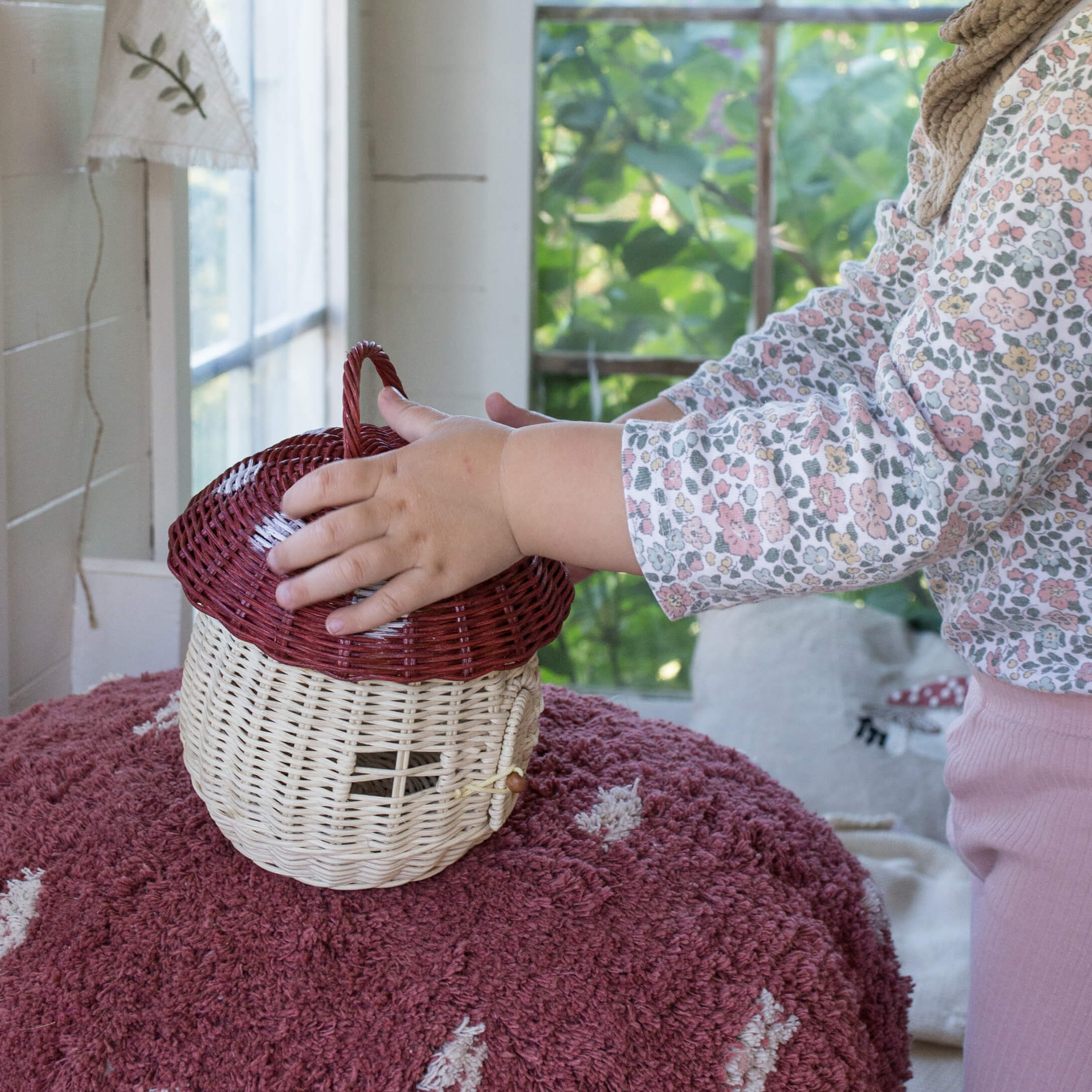 Kind raakt natuurlijke rieten mand in paddenstoelvorm aan op roze vloerkleed binnen