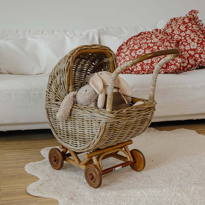 Rieten kinderwagen met houten wielen en knuffels in lichte kamer met witte bank