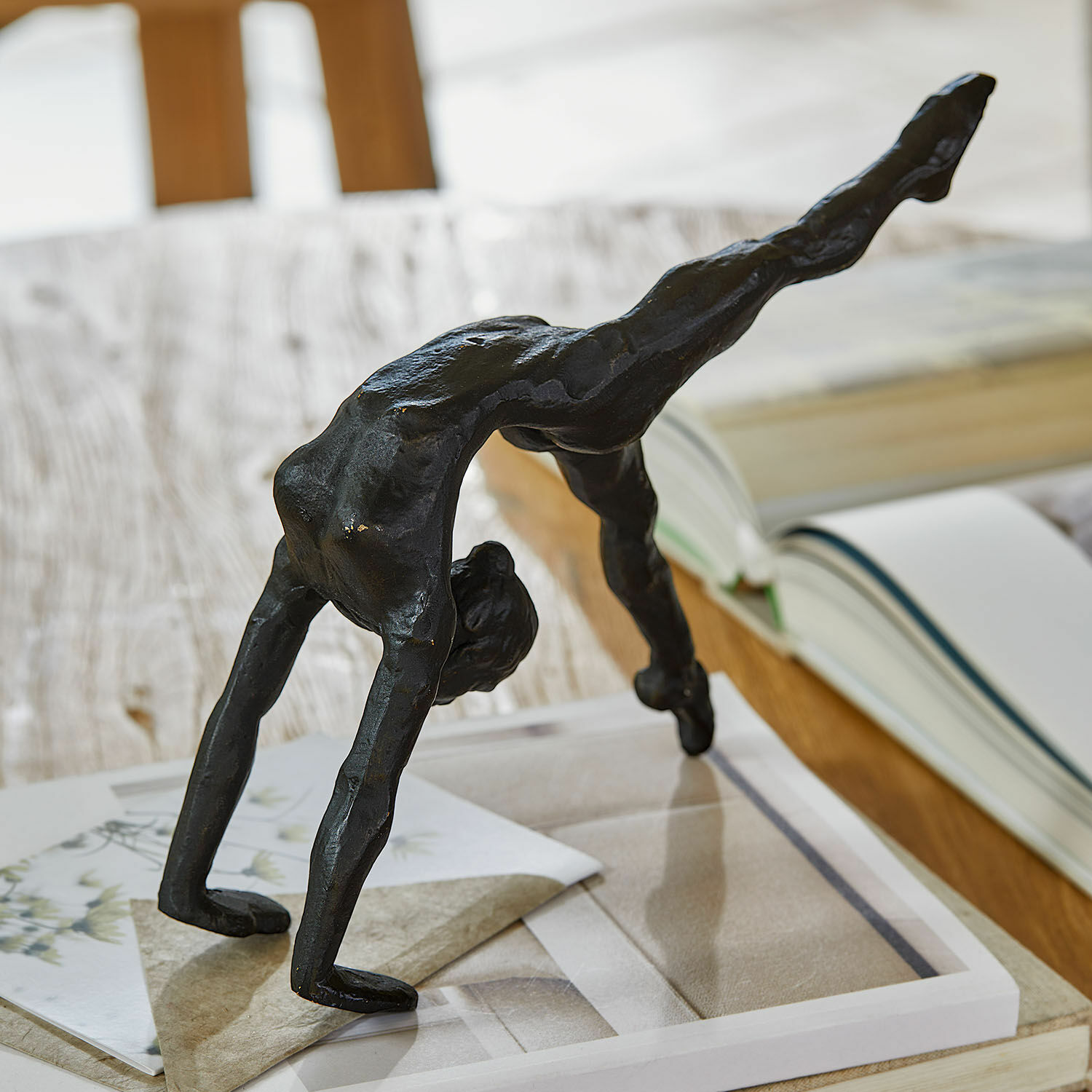 Zwarte metalen beeld van acrobaat in brugpositie op tafel met boeken en papier