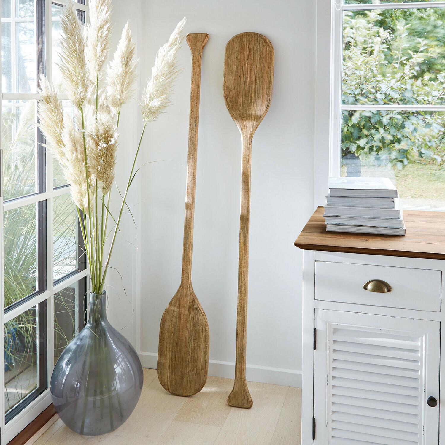Twee decoratieve houten peddels in lichte kamer naast grijze vaas en witte kast