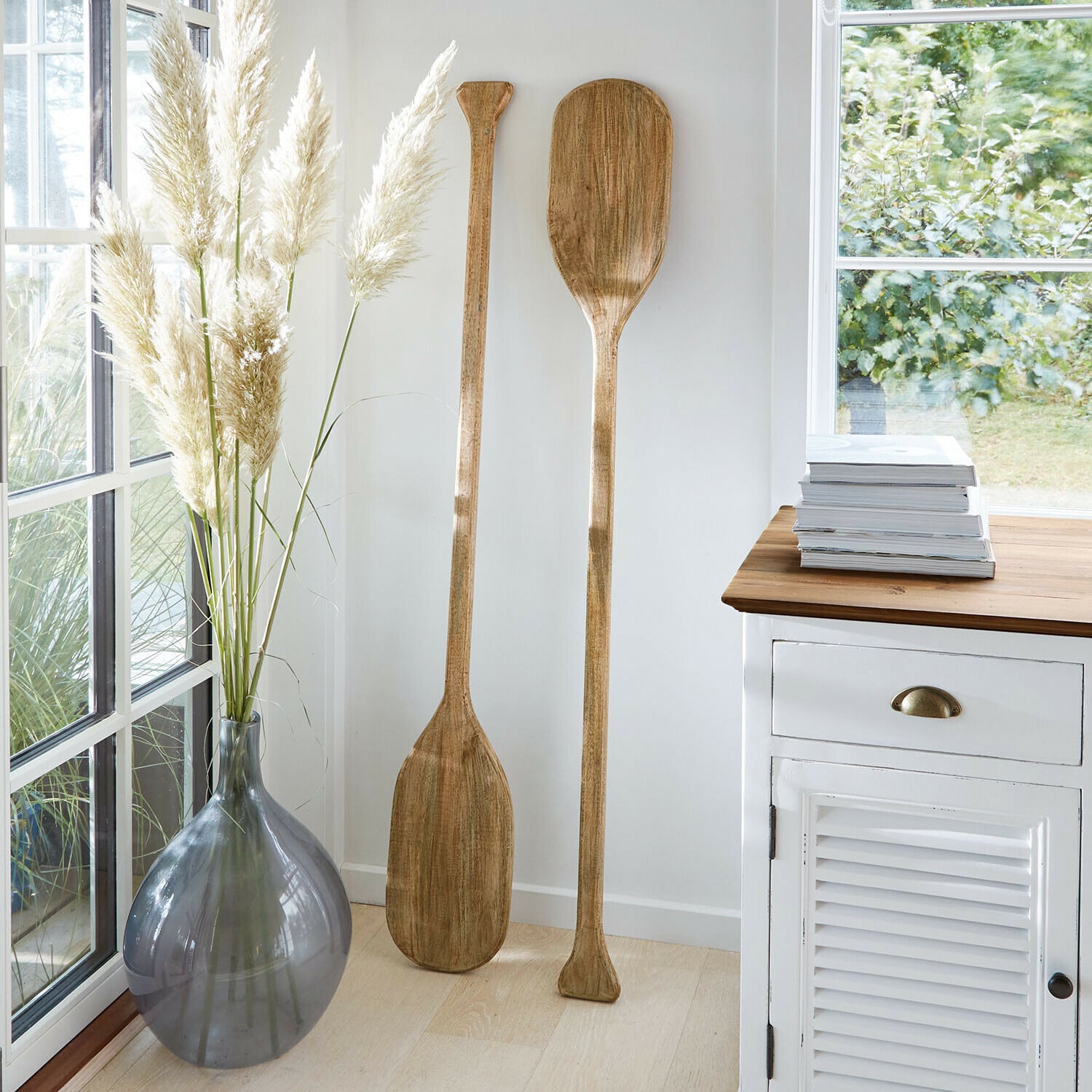 Decoratieve peddel set van 2 Windermount Twee decoratieve houten peddels in lichte kamer naast grijze vaas en witte kast