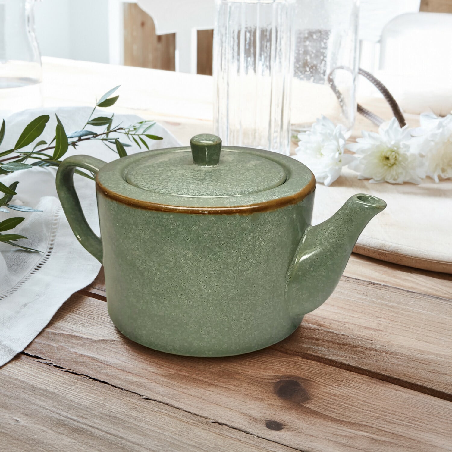 Theepot Biarré Groene keramische theepot met deksel en bruine rand op houten tafel met bloemendecoratie