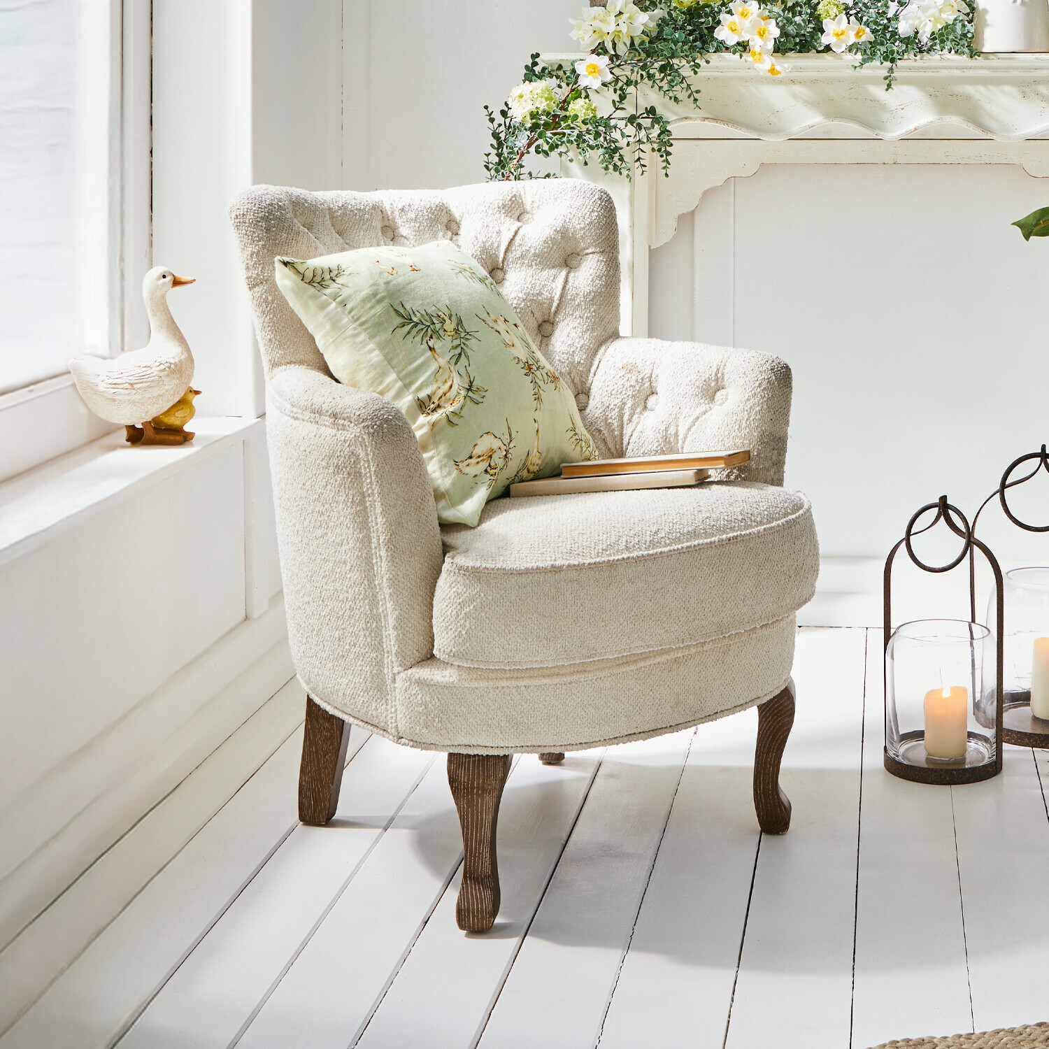 Beige fauteuil van zachte stof met houten poten en groen bloemenkussen in lichte kamer