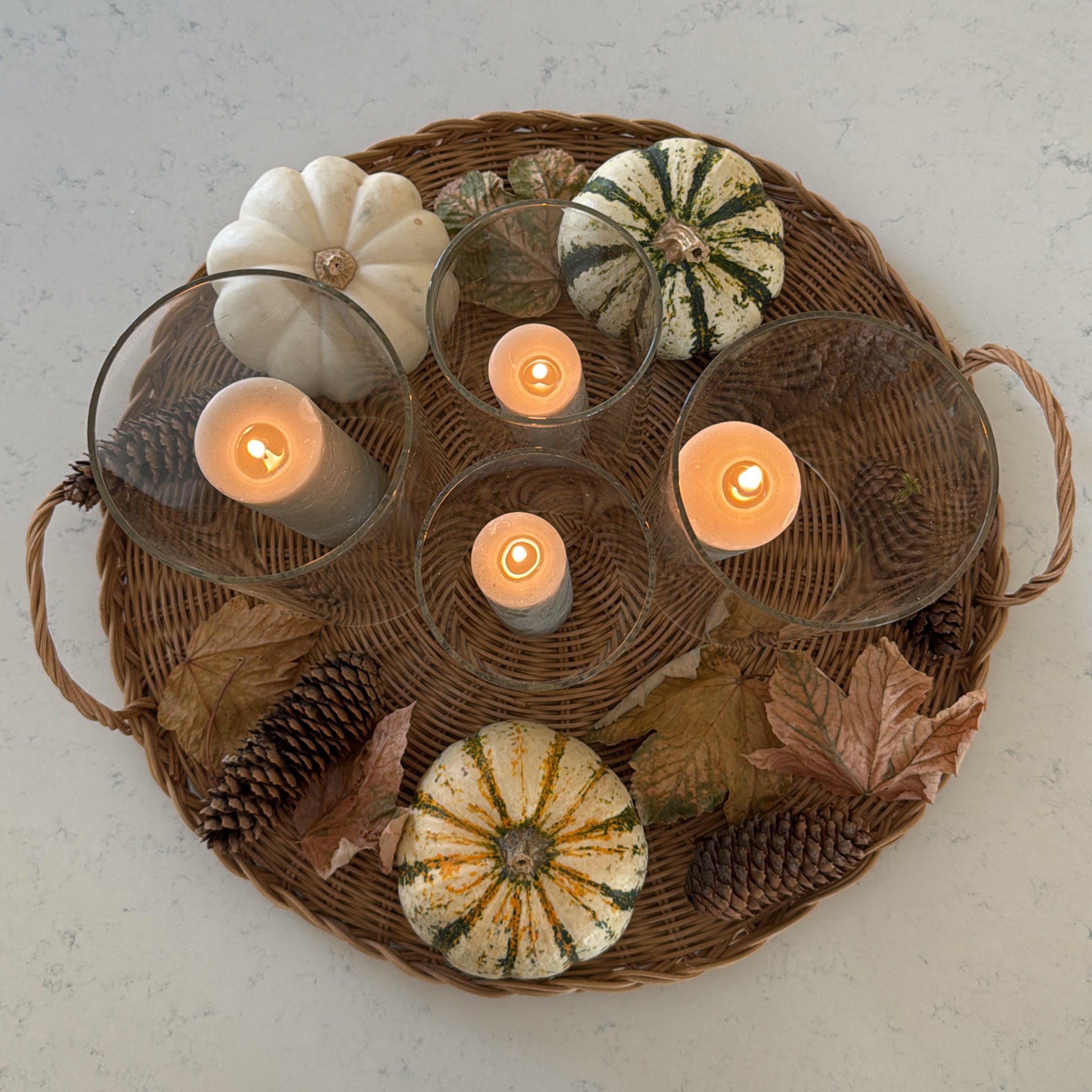 Herfstdecoratie met pompoenen, dennenappels en kaarsen in glazen houders op een rieten dienblad