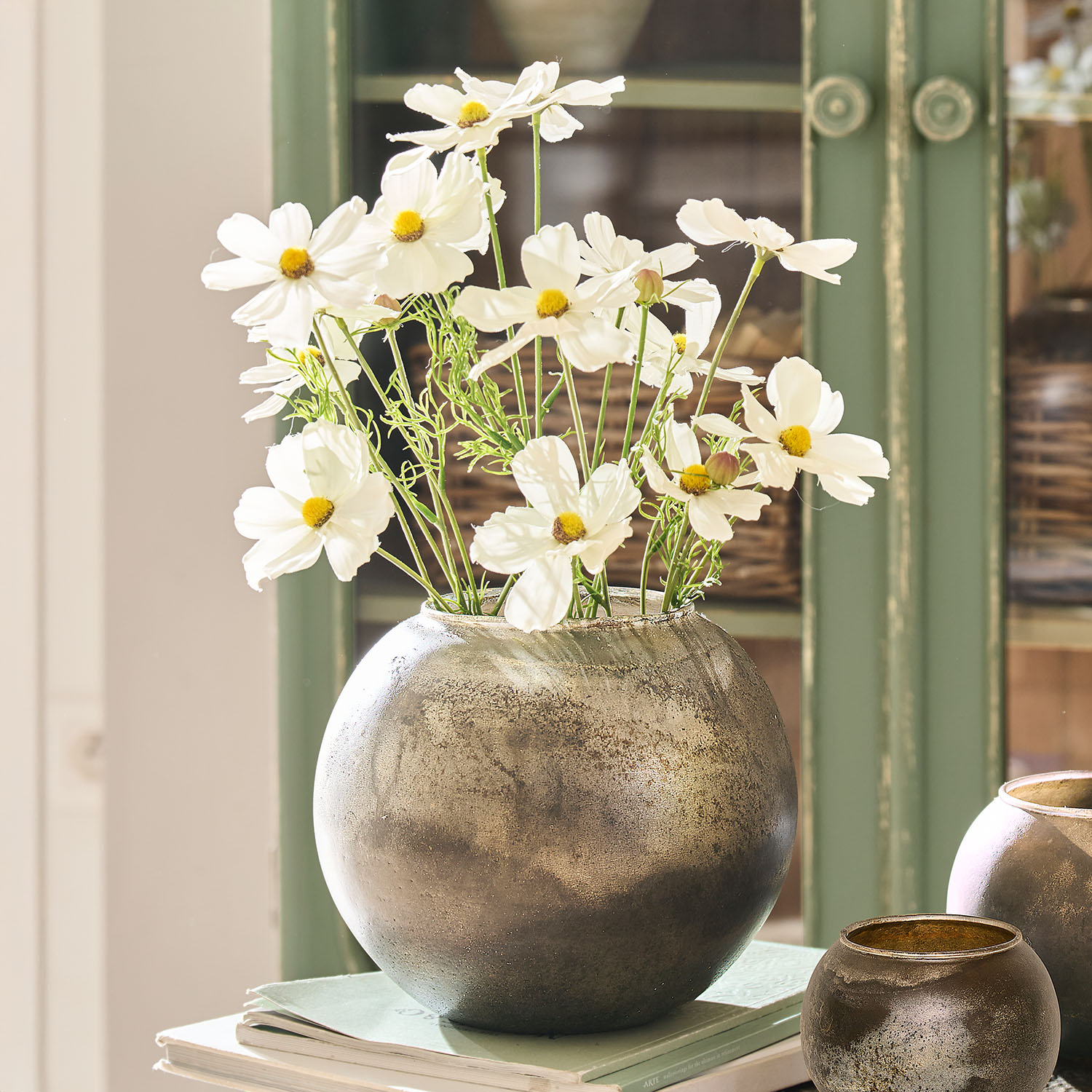 Ronde zilverkleurige metalen vaas met witte bloemen op boeken, stijlvolle interieurdecoratie