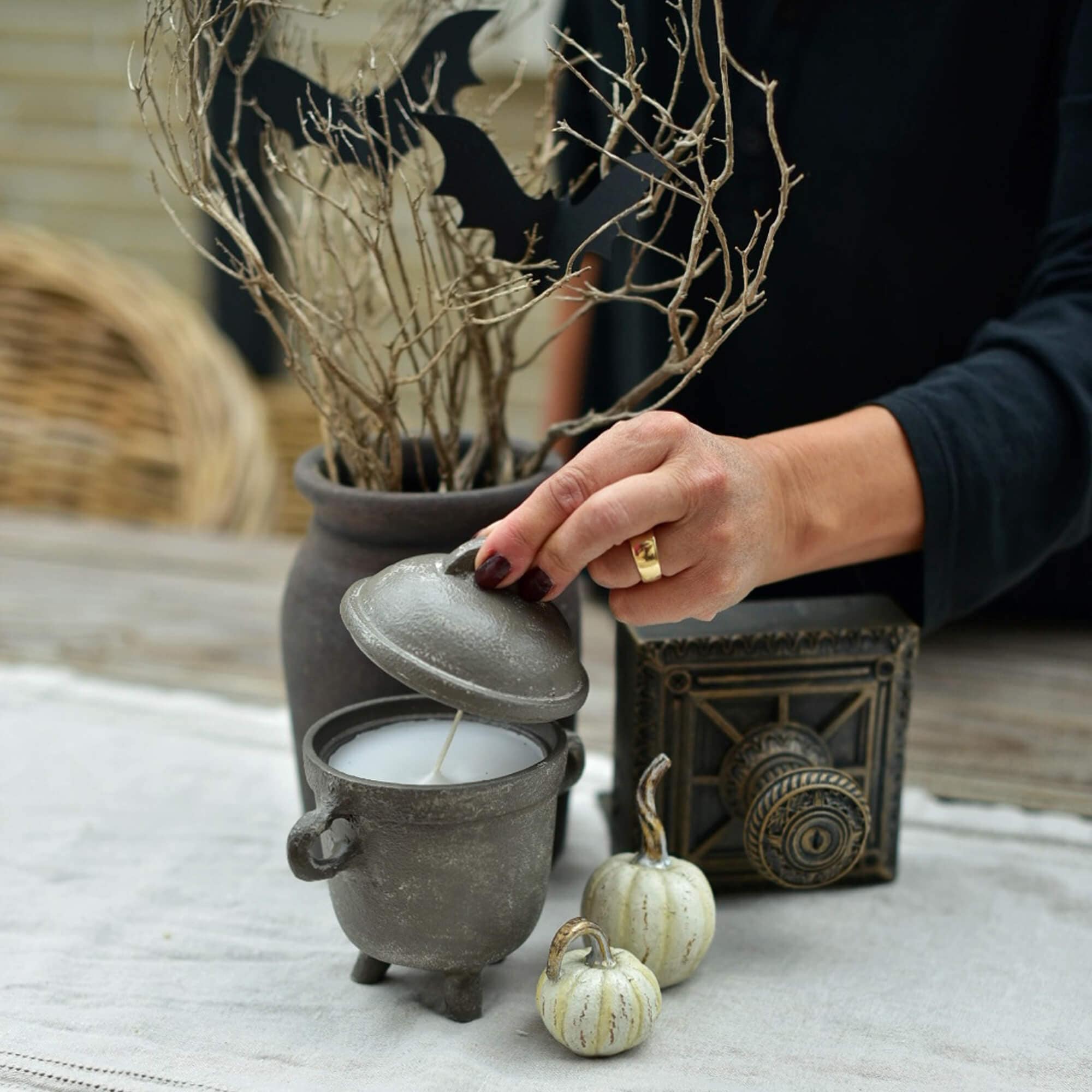 Grijze kaars in ketelvorm met deksel op Halloween-tafel met pompoen- en takdecoraties