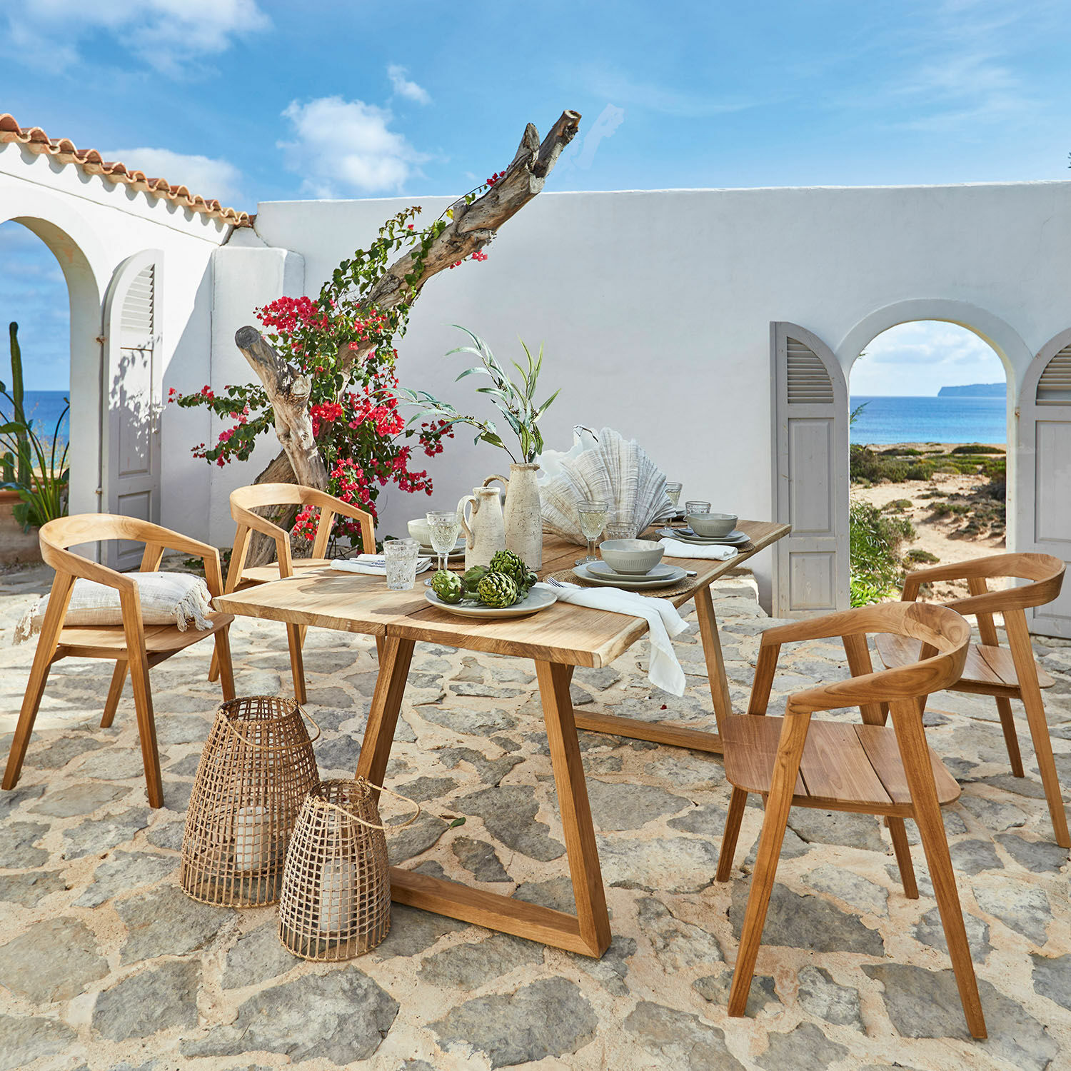 Tafel Saulny Tuinmeubelset van teakhout met stoelen en tafel op stenen terras met uitzicht op zee