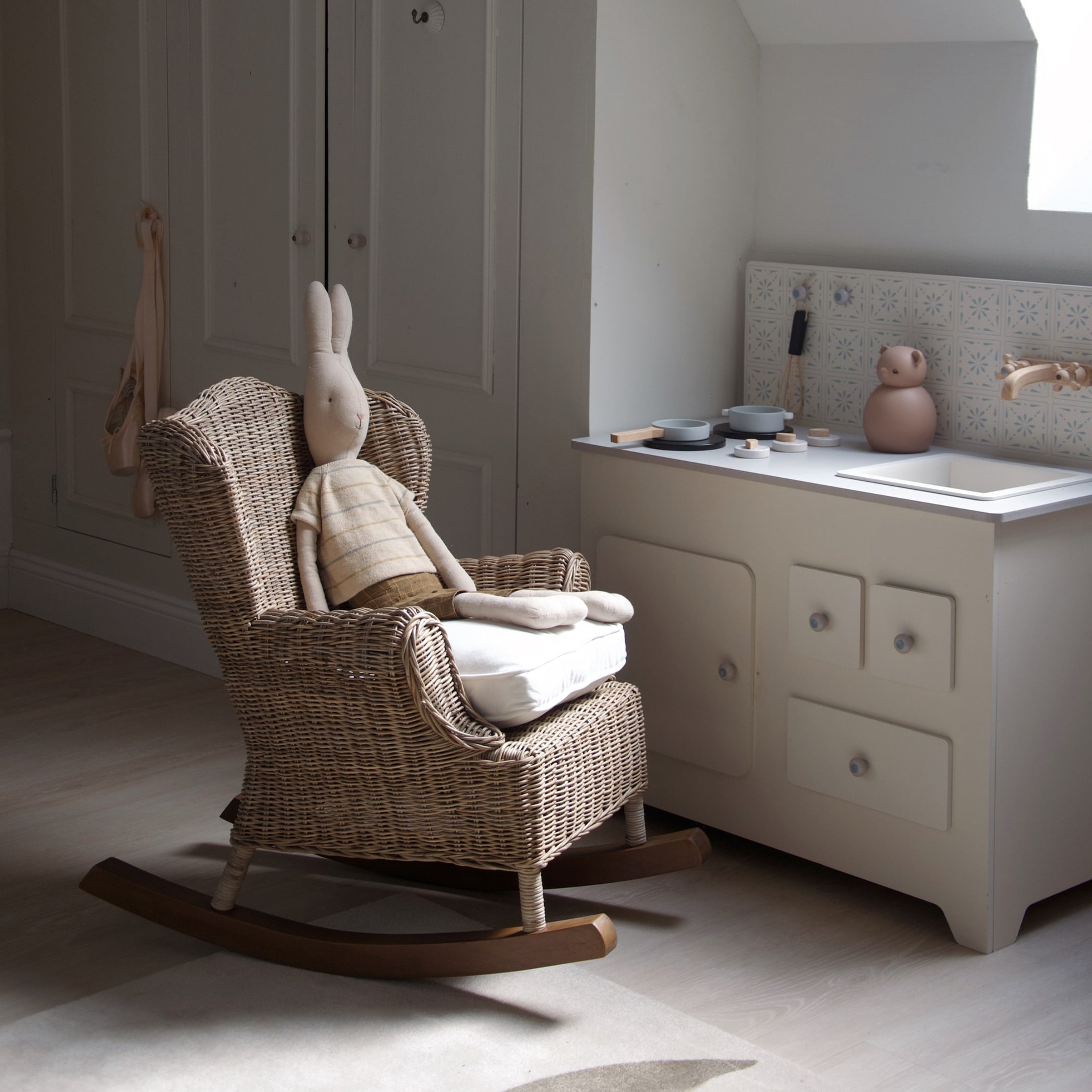 Kinder schommelstoel van riet met licht kussen en beige knuffelkonijn in lichte kleding