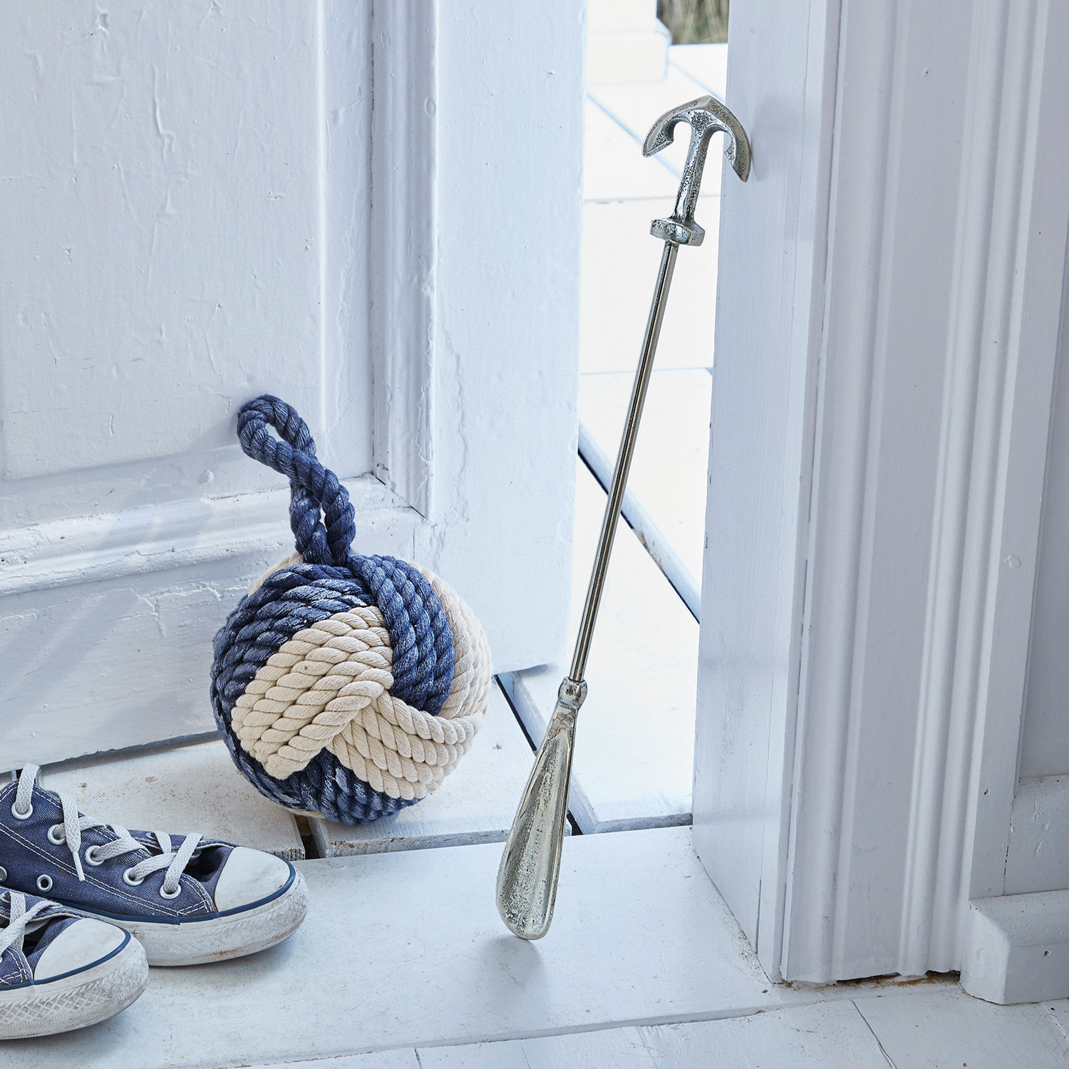 Schoenlepel Priam Metalen deurstop in anker vorm met blauw-beige touwgewicht op witte vloer